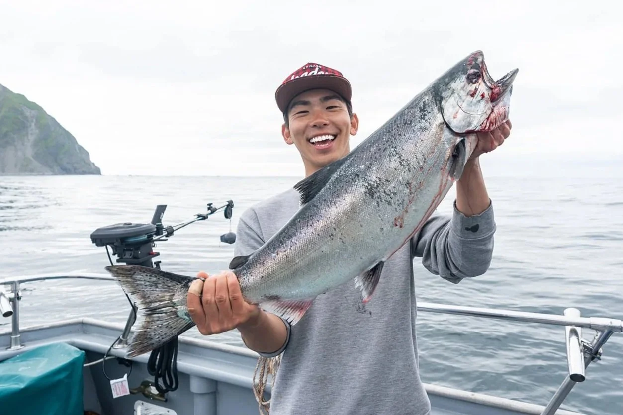 Young man holding a large king salmon fish on a boat in the water.