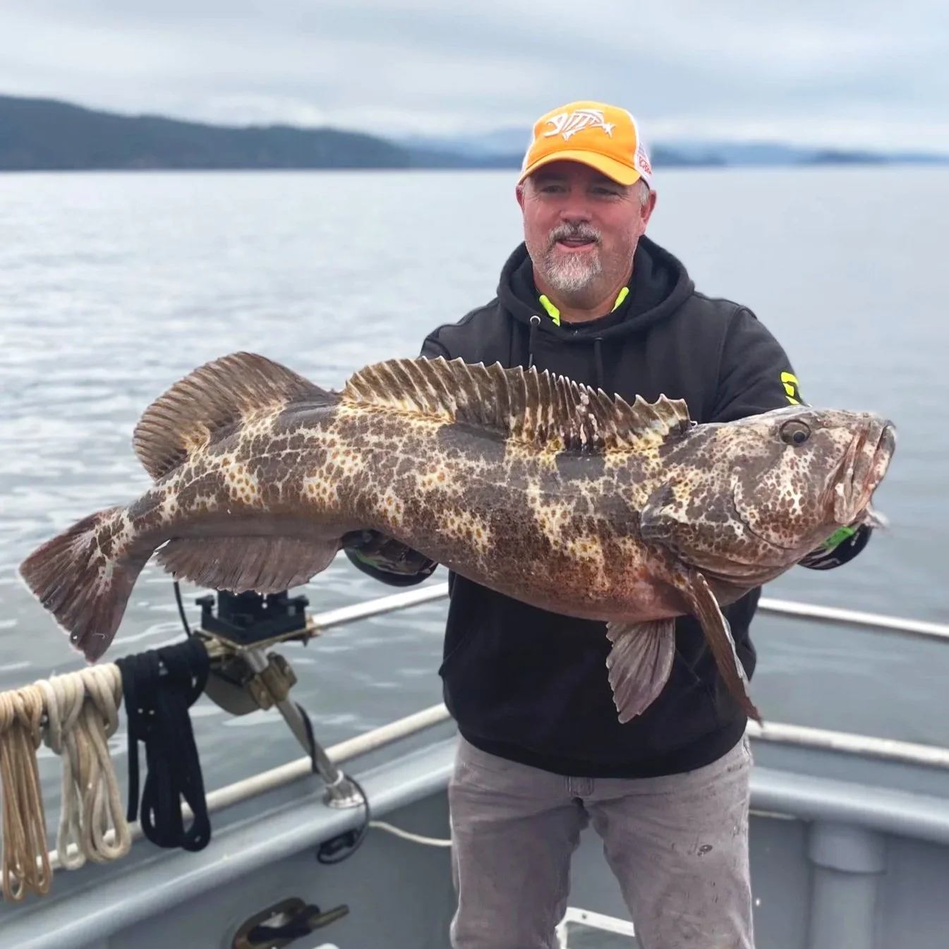 Man holding a large red and brown fish on a boat with water and distant shoreline in the background.