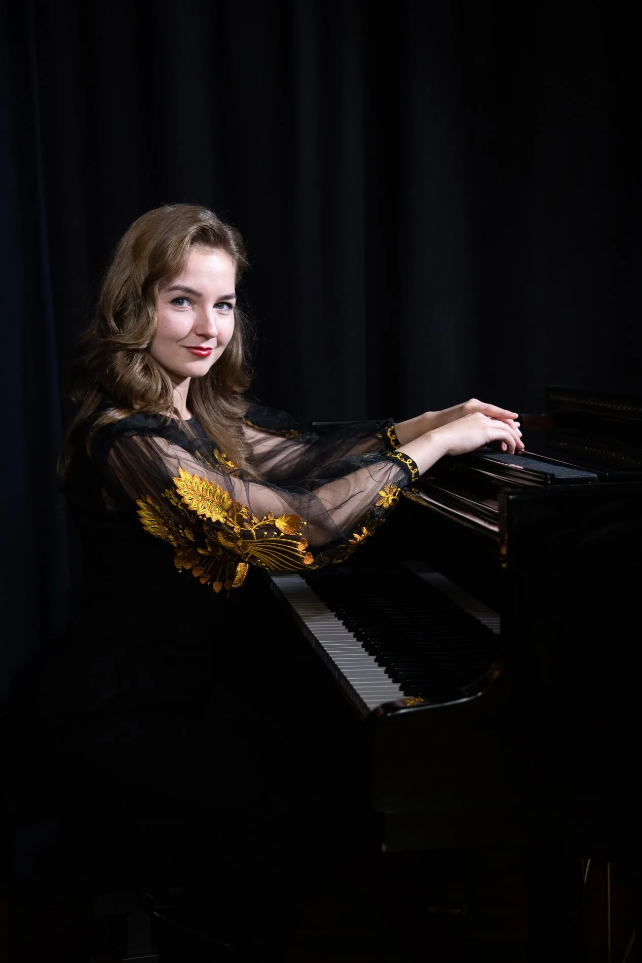 Junge Frau spielt Klavier auf einer schwarzen Bühne mit schwarzen Vorhängen im Hintergrund.