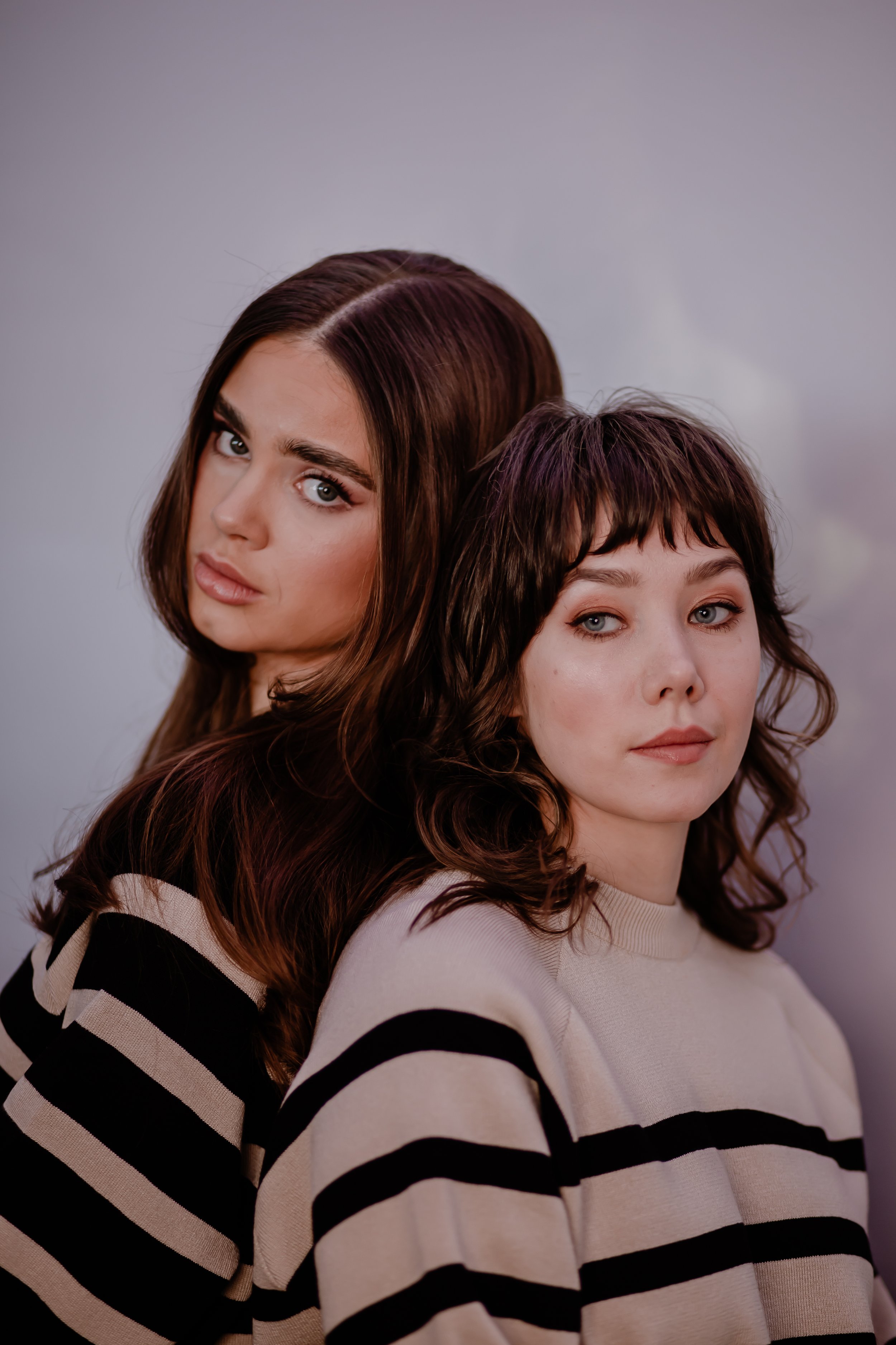 two brown haired girls posing for a camera wearing striped jumpers