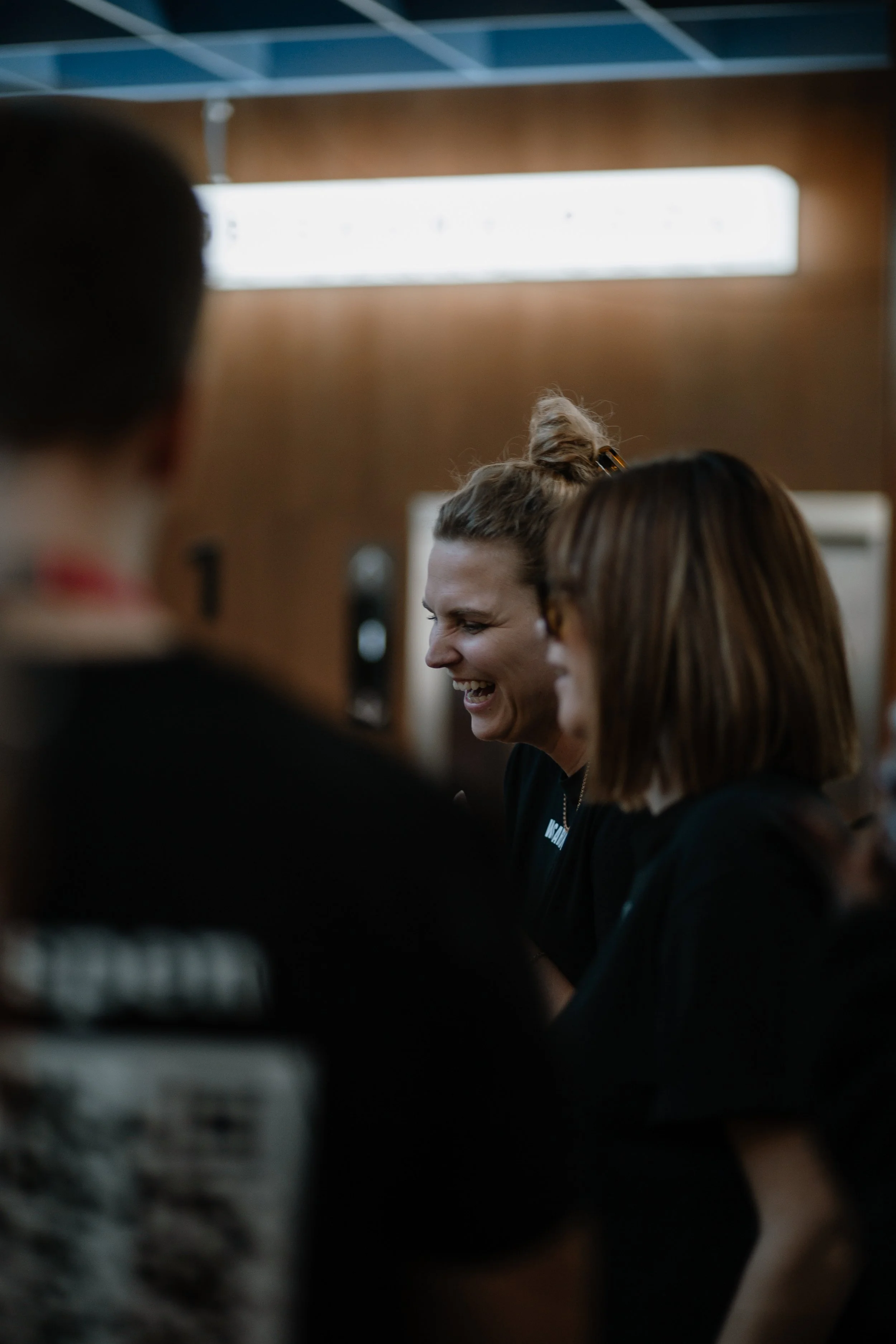 Group of people laughing and talking indoors, with a woman in the center smiling.