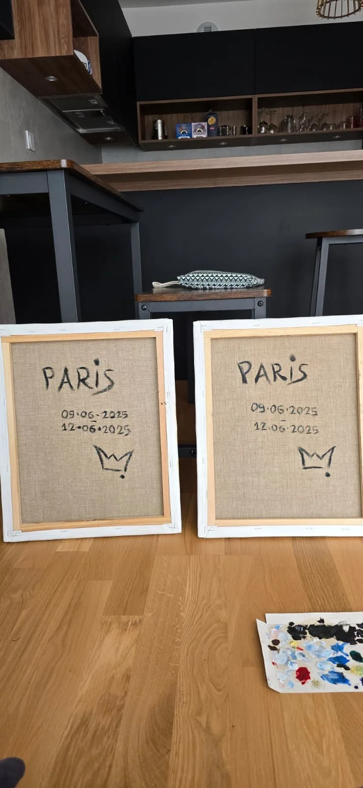 Two blank canvases with handwritten text and a crown drawing, placed on a wooden table in a kitchen or dining area, with a paint palette nearby.