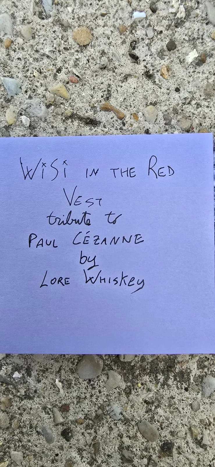 A handwritten note on a purple piece of paper resting on a rough, sandy surface. The note reads: 'Wish in the Red Vest tribute to Paul Cézanne by Lore Whiskey.'