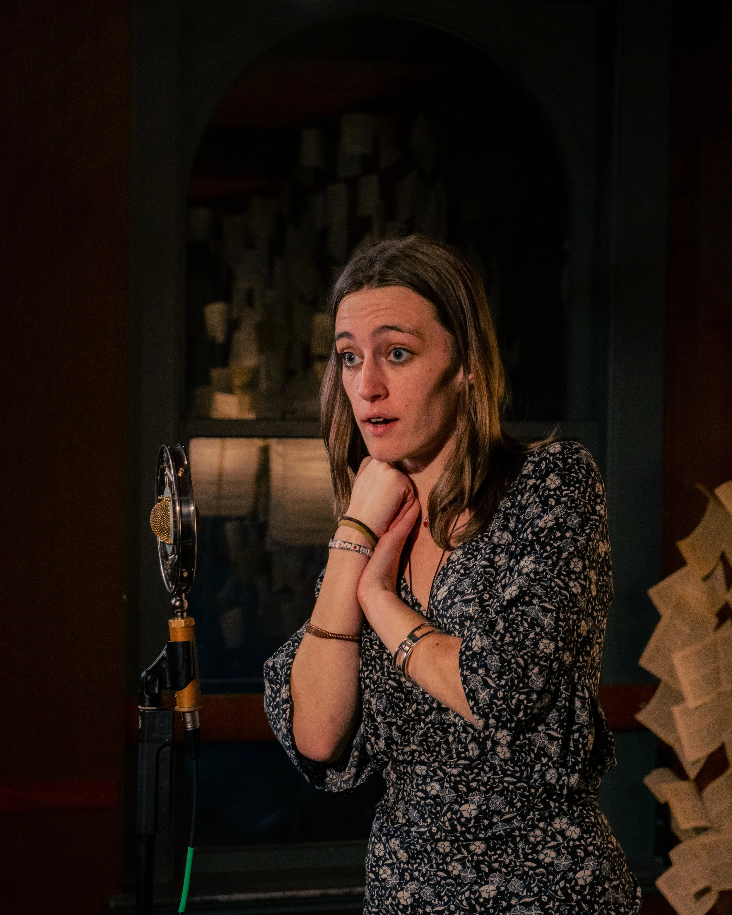 A young woman singing into a vintage microphone in a recording studio.