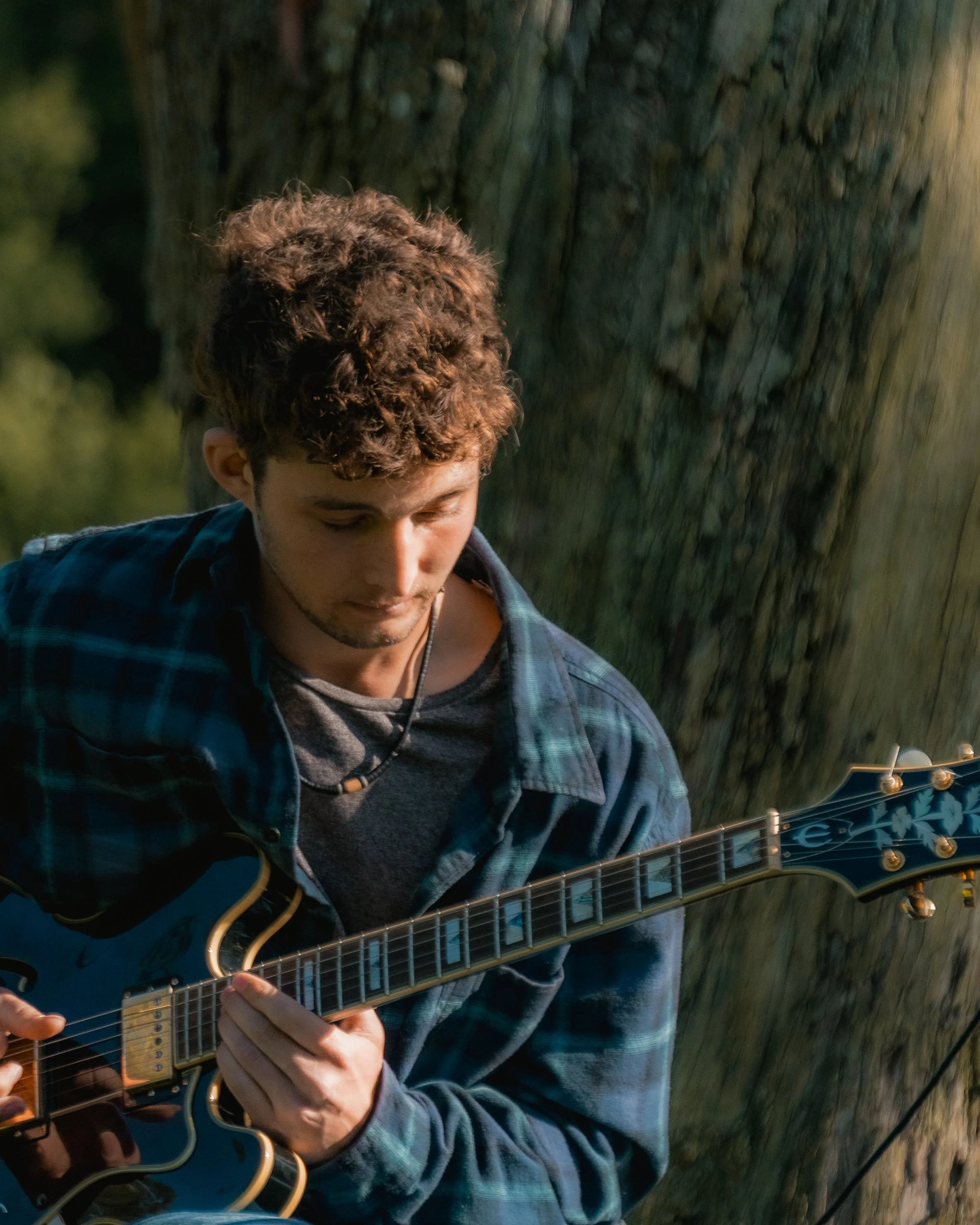 A young man with curly hair playing an electric guitar outdoors.