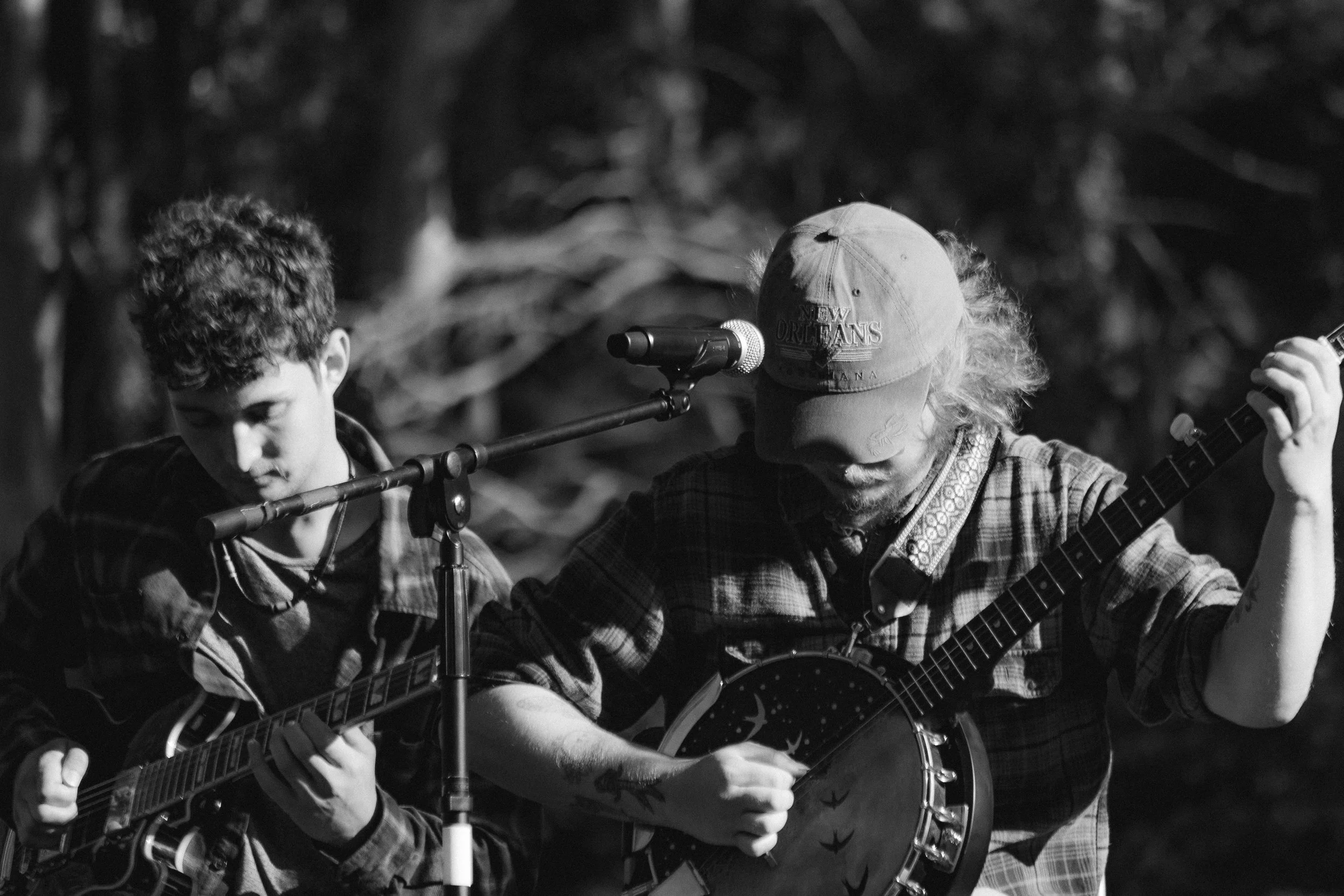 Two musicians playing guitars outdoors, one with a harmonica, in black and white.