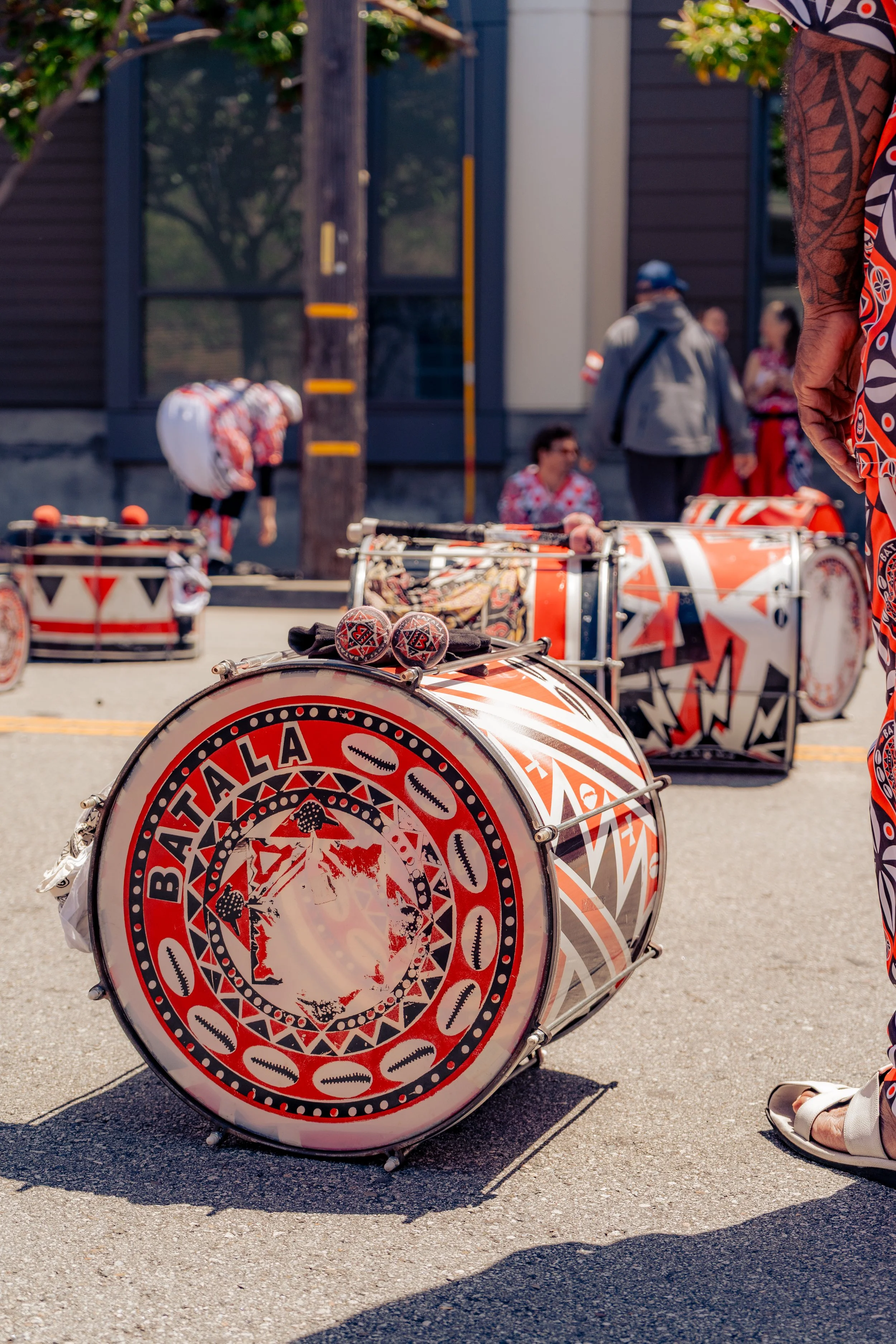 Colorful drums with traditional indigenous patterns and the word 'BATAALA' on the front, set up outdoors on a street.