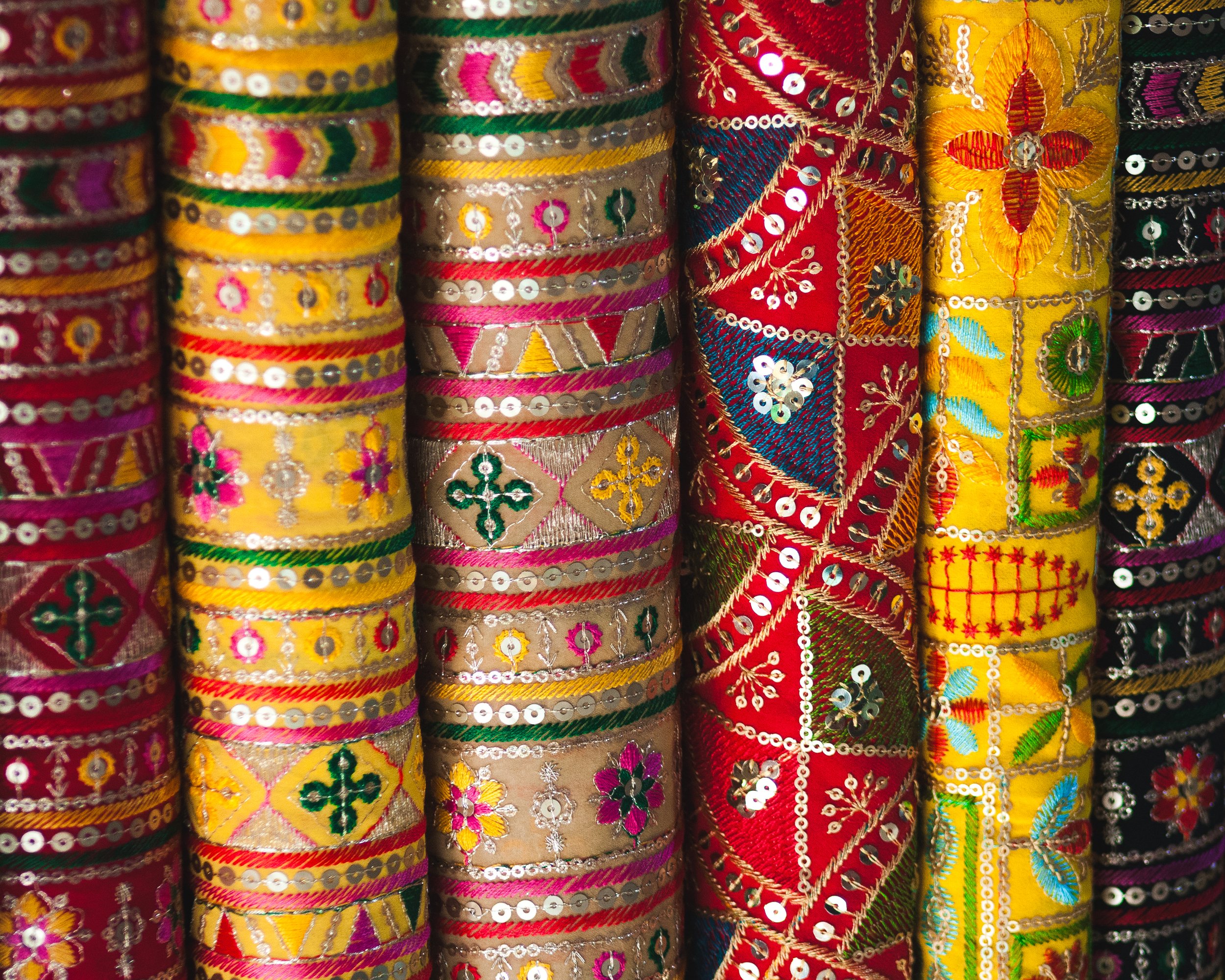 Rolls of colorful embroidered and sequined fabric trims with floral and geometric patterns.