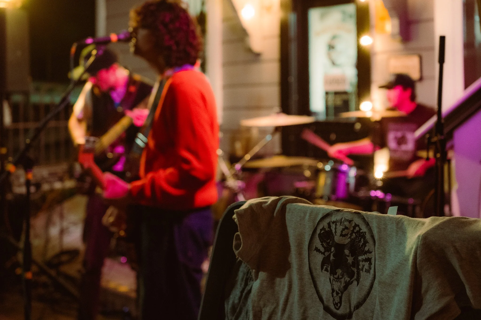 A group of musicians performing live at an outdoor venue at night, with a focus on a cloth with a tree logo hanging on a chair in the foreground.