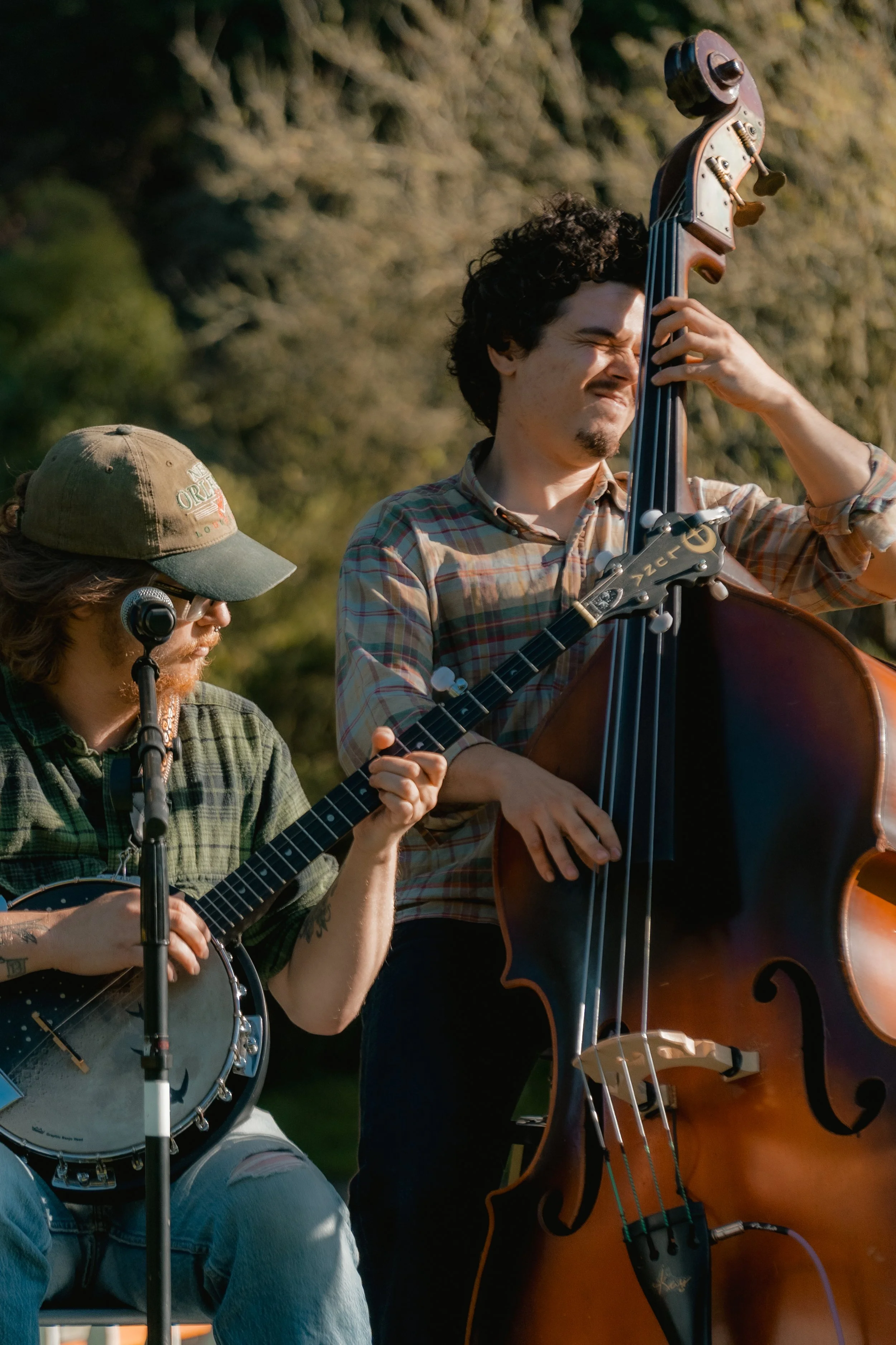 Two musicians playing guitars outdoors during sunset, one with a banjo and the other with a double bass.