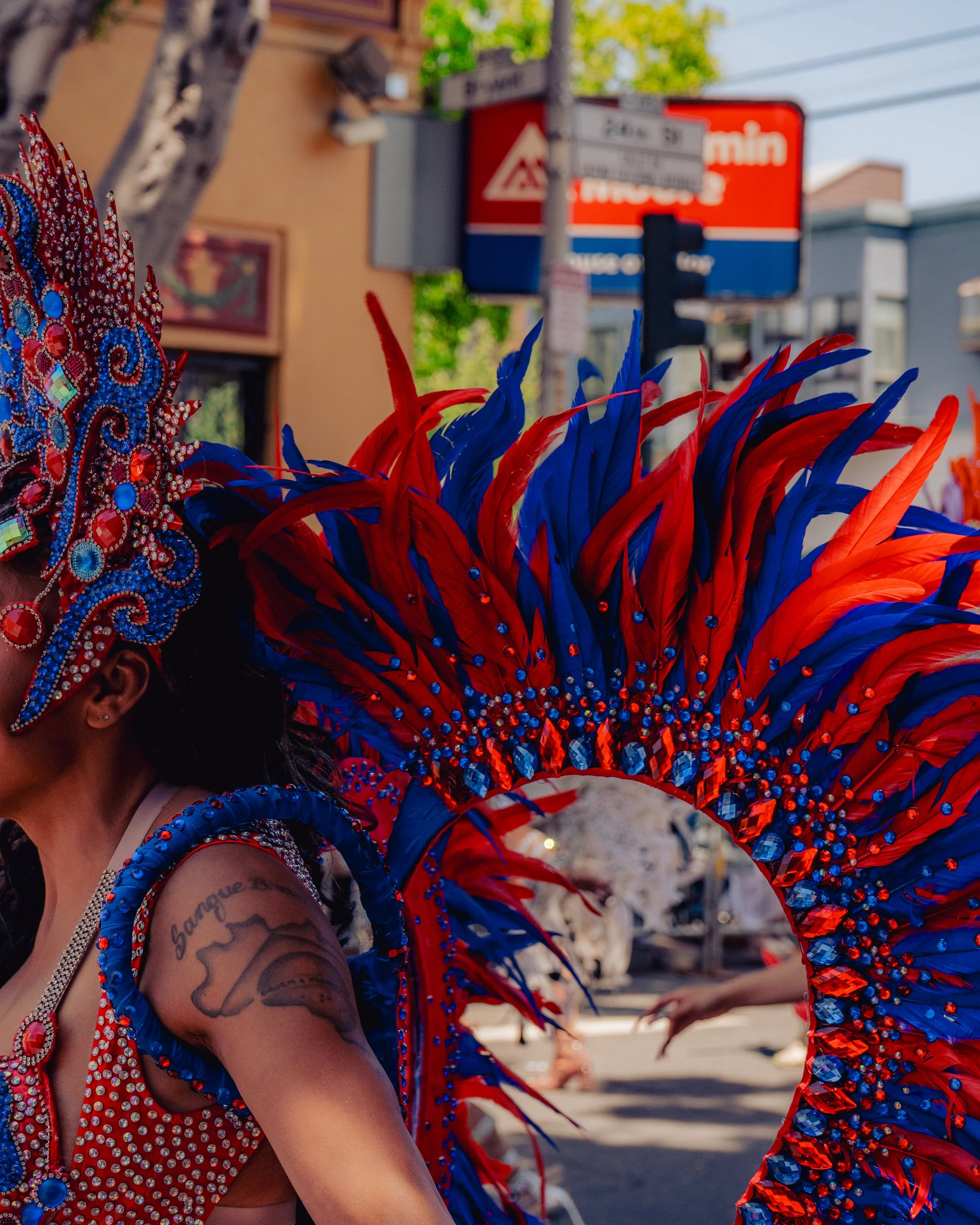 Woman dressed in a vibrant red and blue carnival costume with feathers and rhinestones, participating in a parade or festival