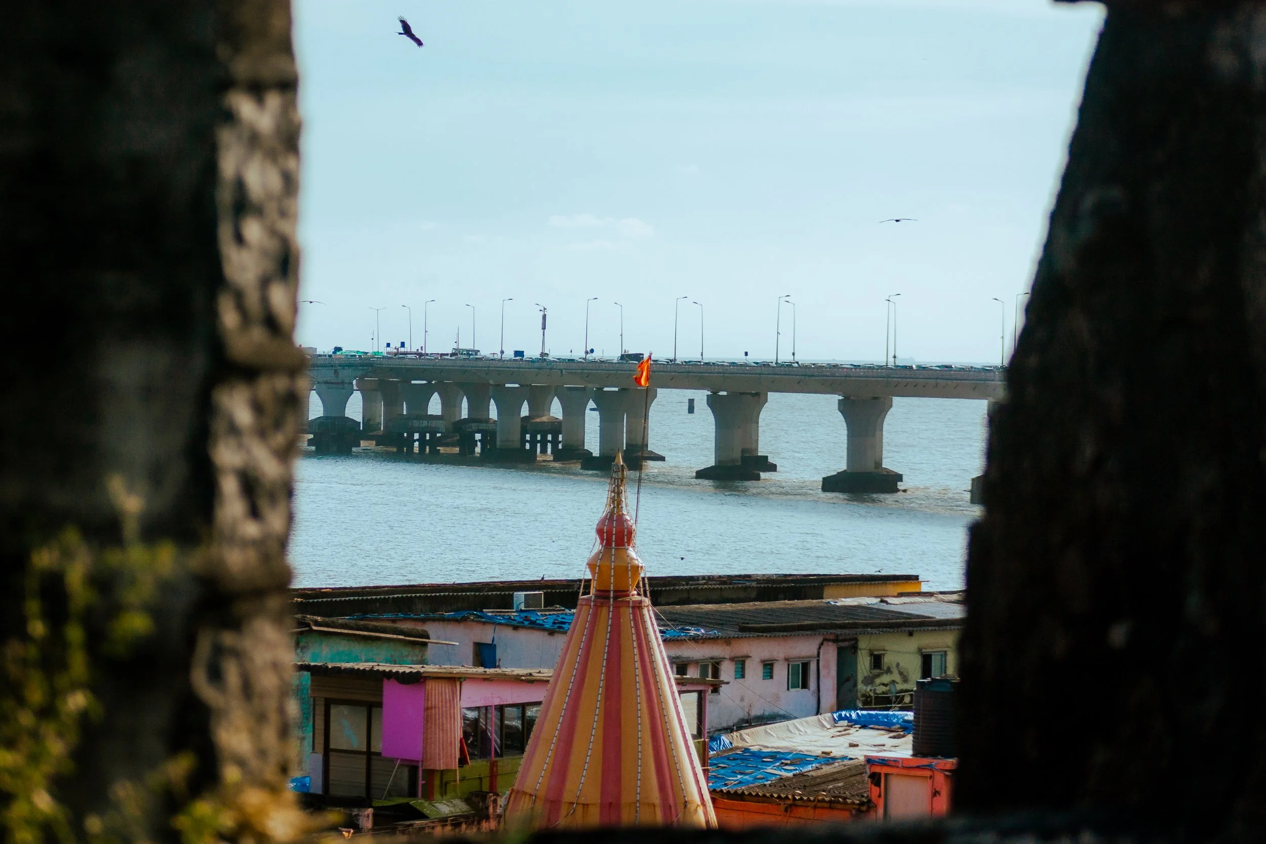 View of a bridge over water as seen through a window with a staircase and small buildings in the foreground.