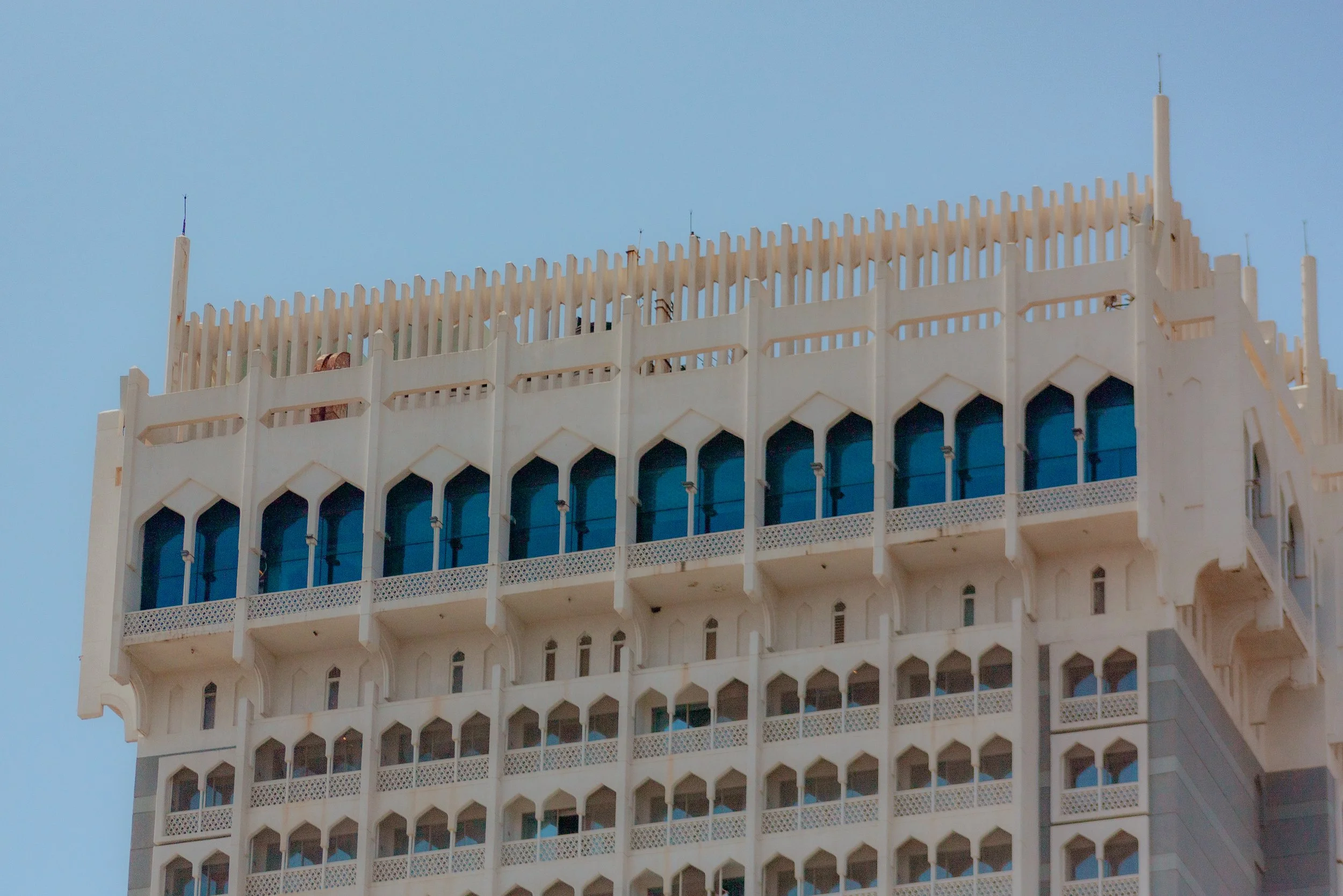 Close-up of a high-rise building with Gothic-style arched windows and a white facade, topped with decorative spires against a clear blue sky.