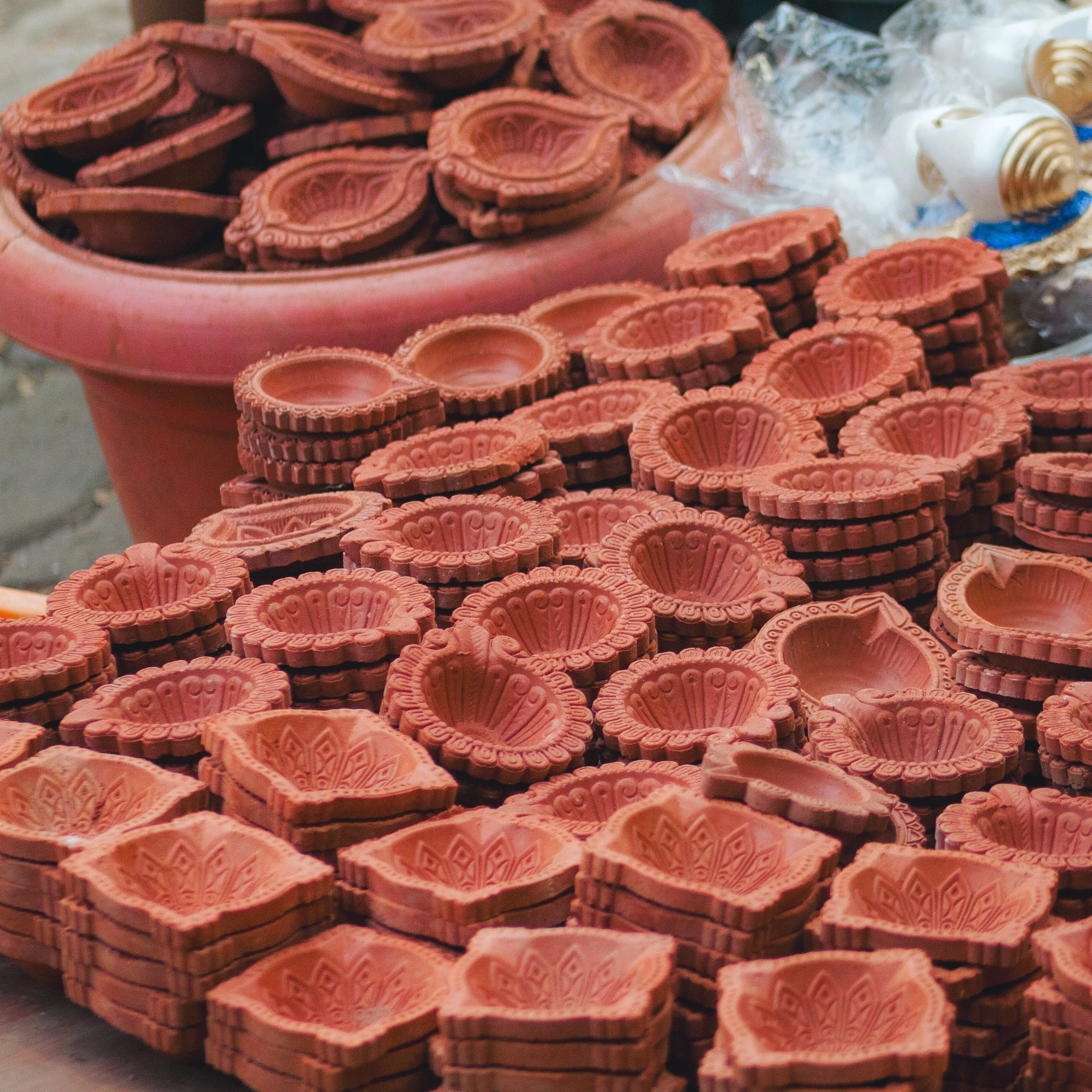Stacked orange terracotta prayer or incense holders with intricate carved designs, displayed on a table, likely at a market or shop.