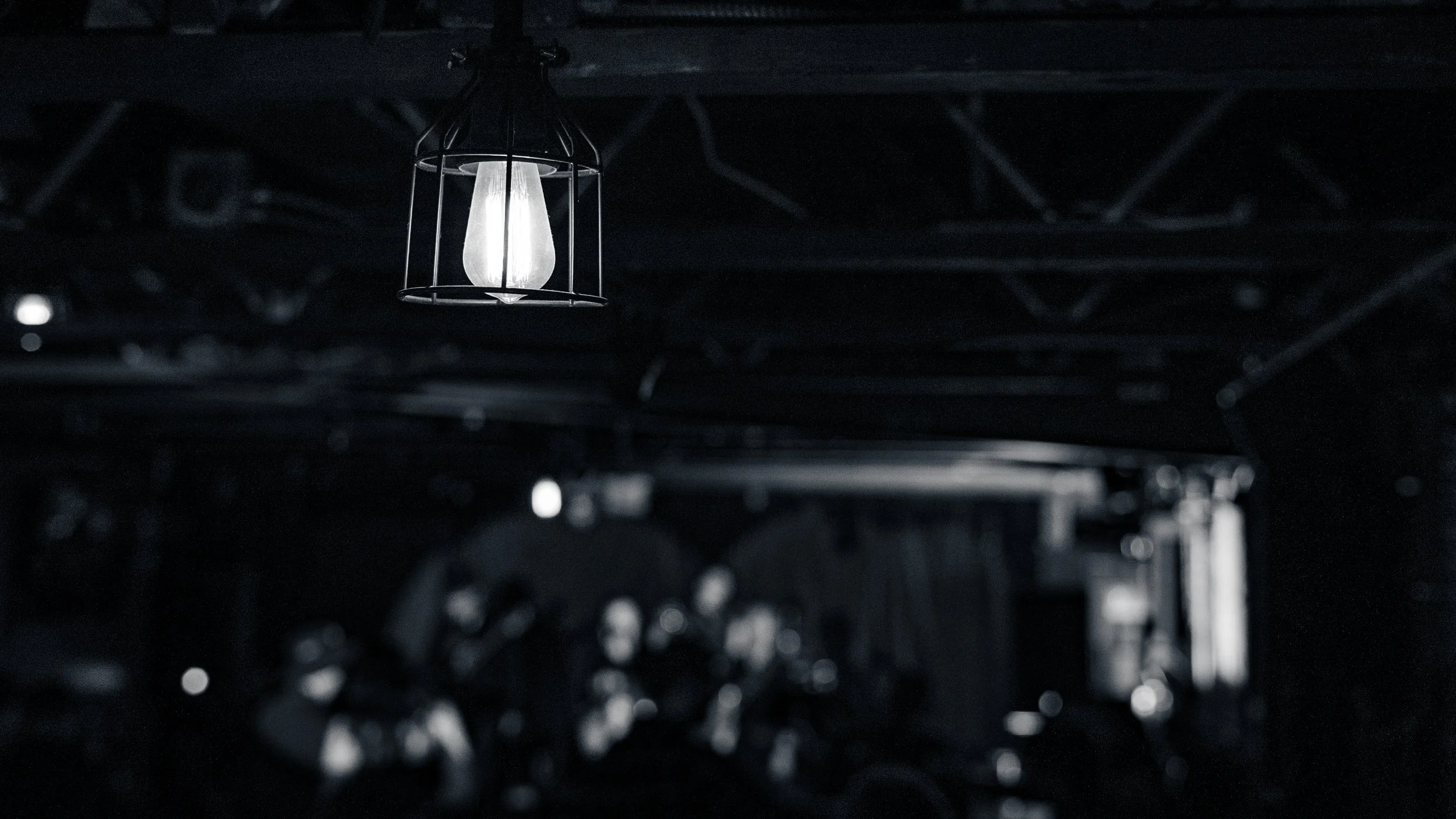 A single industrial-style light bulb in a cage hanging from a dark ceiling.