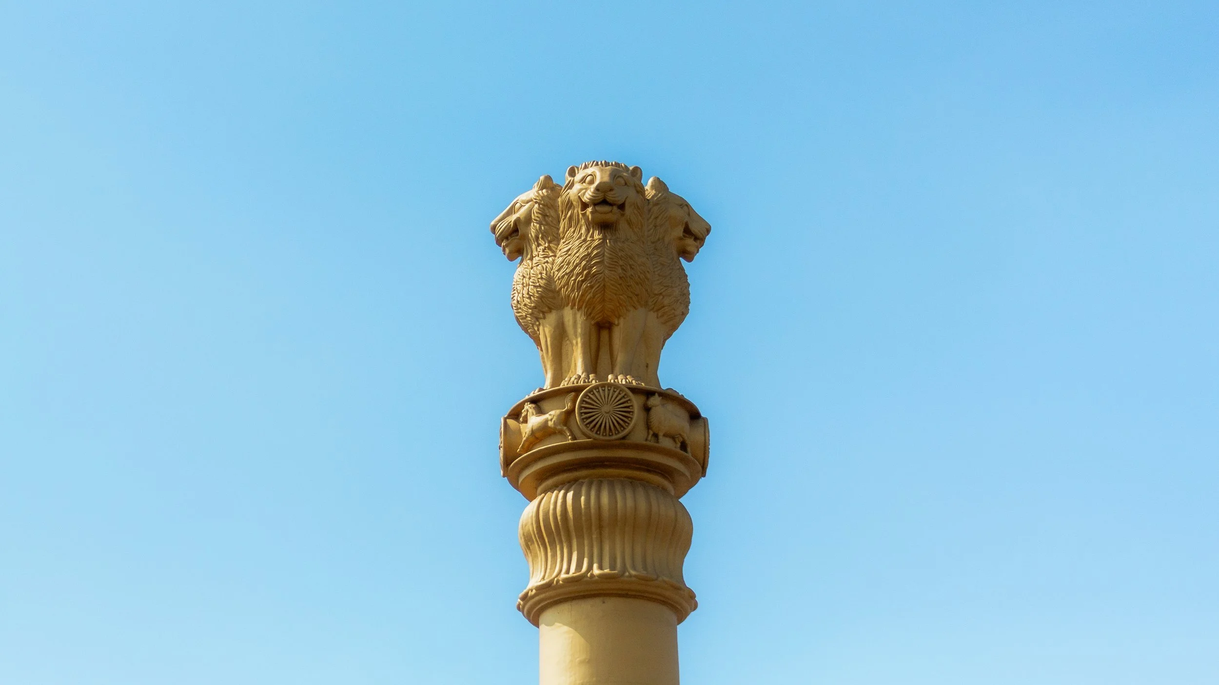 A tall pillar topped with a sculpture of four lions standing back to back against a clear blue sky.