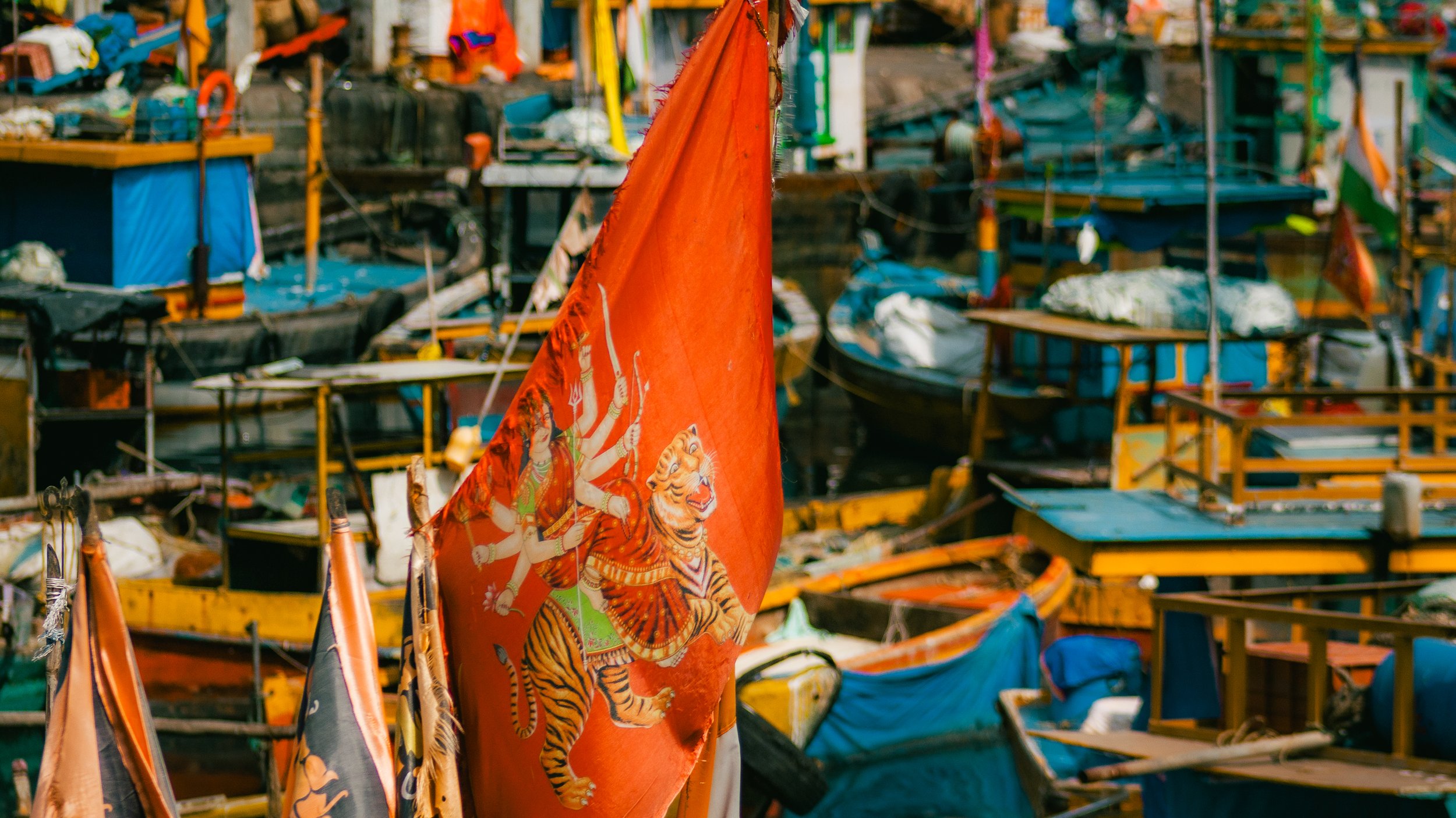 A red flag with a Hindu goddess riding a tiger, surrounded by boats and floating houses in a waterway.