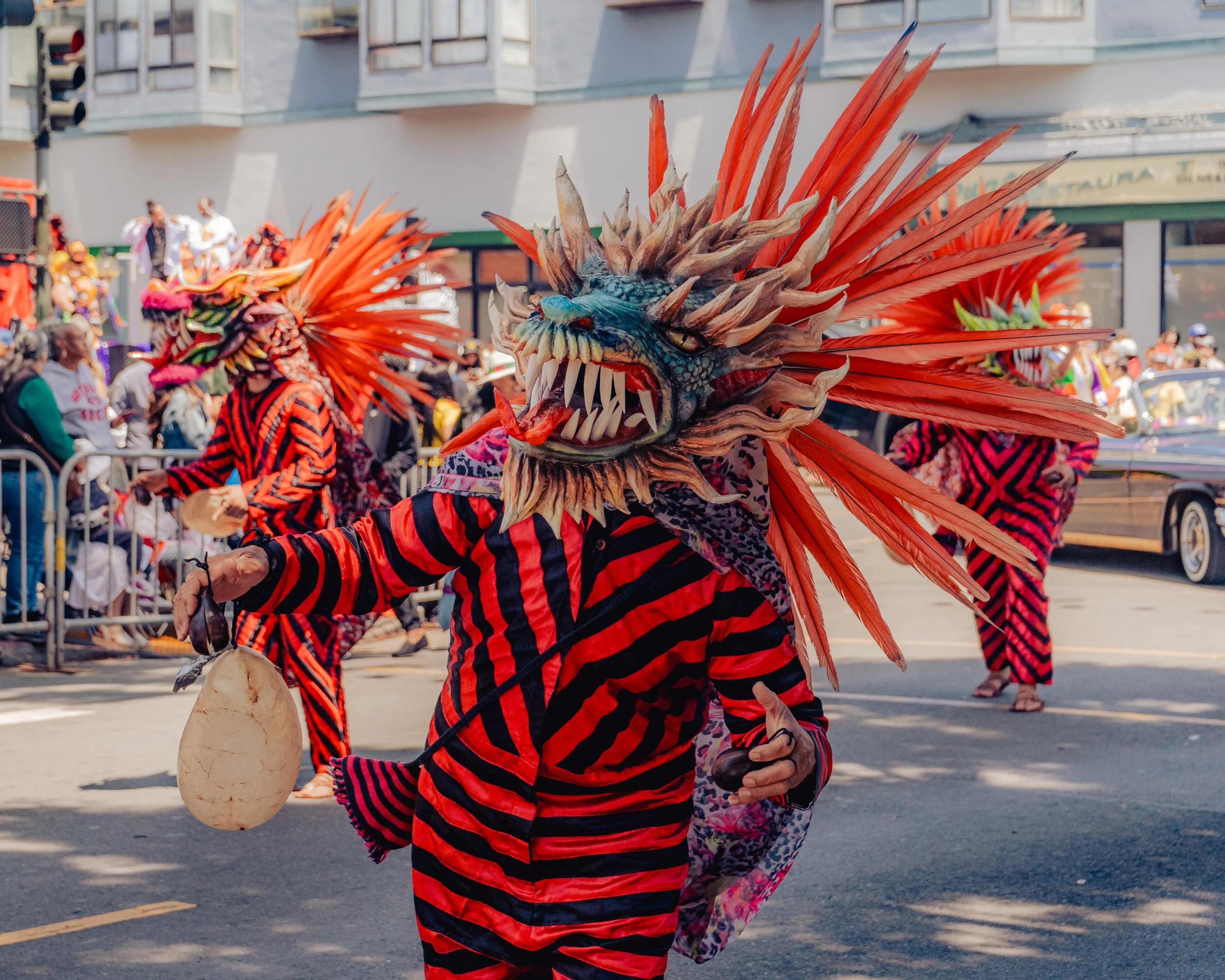People in colorful costumes with dragon masks participating in a parade on a city street.