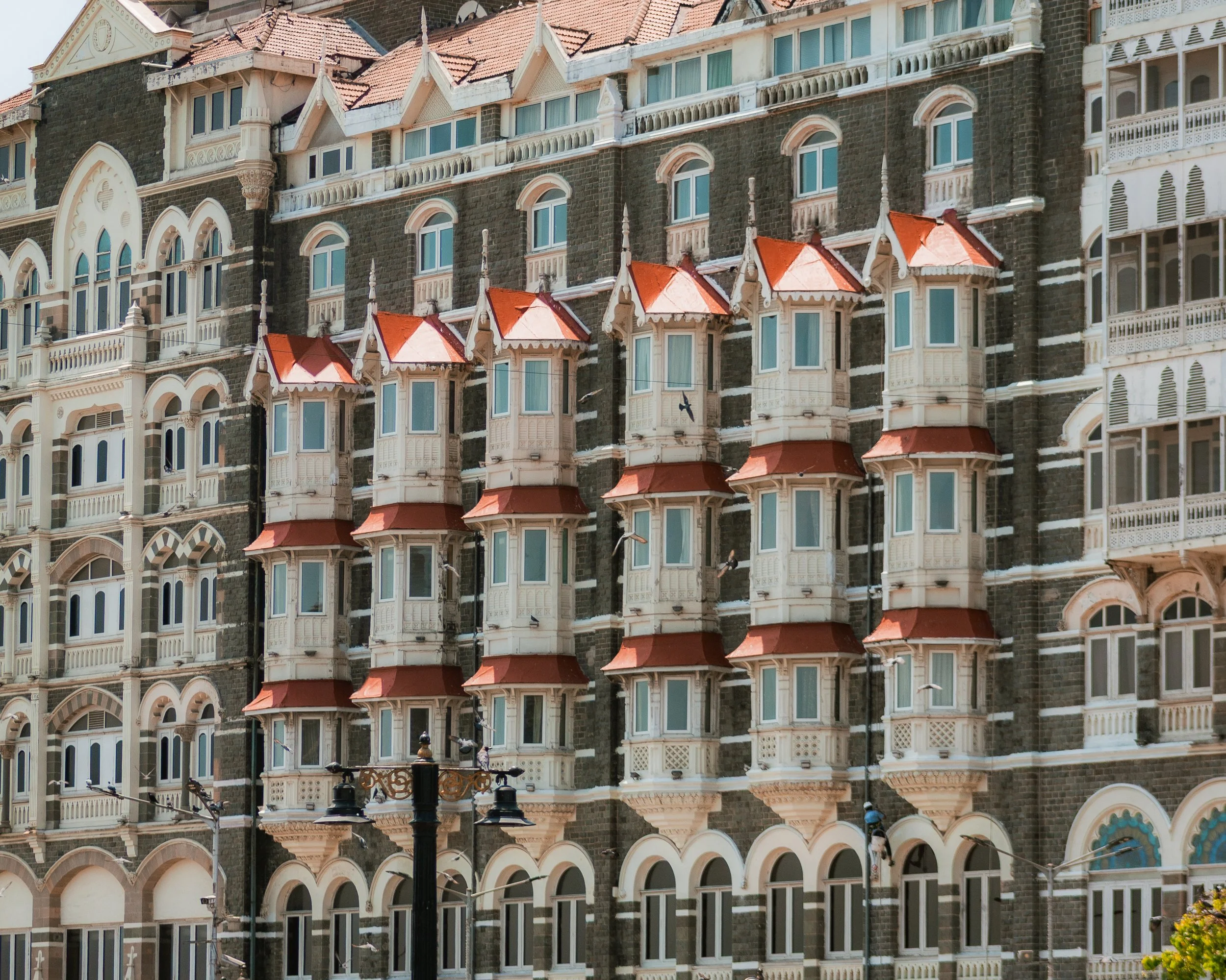 A large multi-story building with Victorian-style tin balconies and turrets, decorated with red and white roofing, black brick walls, and arched windows.