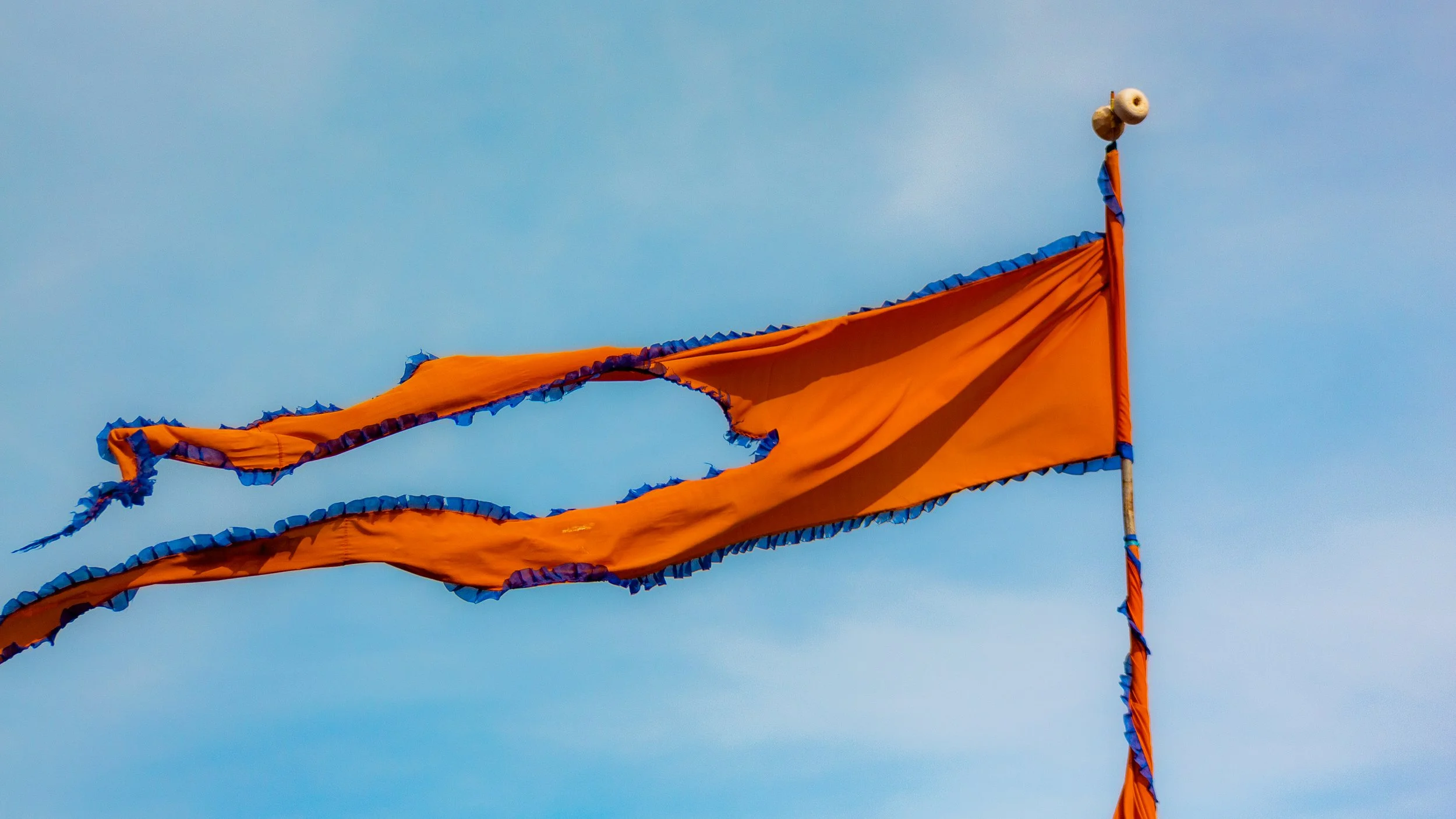 Orange flags with blue trim waving in the wind against a blue sky.