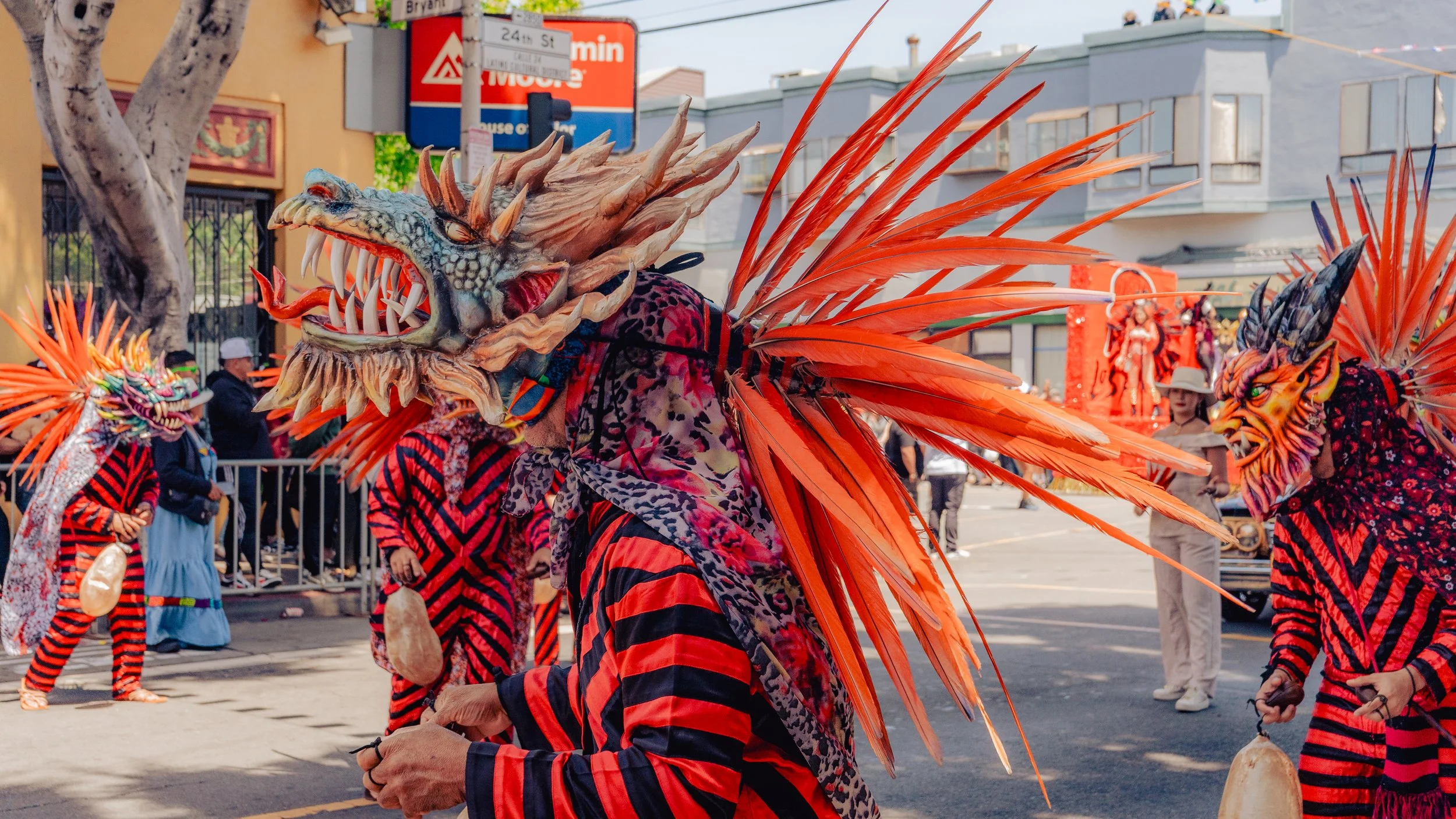 People in colorful costumes and elaborate masks participating in a parade on a city street.