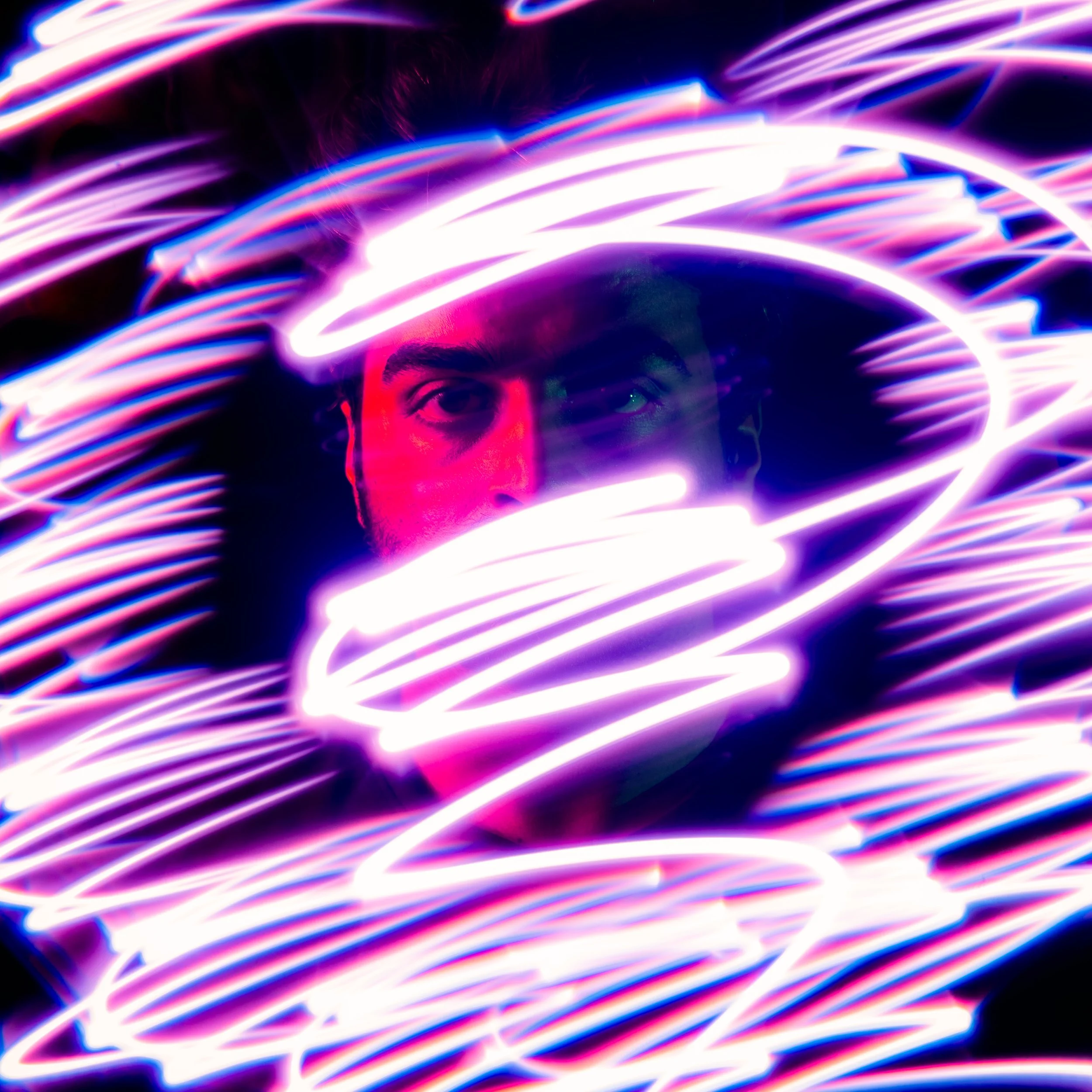 A person with dark hair and focused eyes partially visible behind pink and purple light streaks from long exposure light trails.