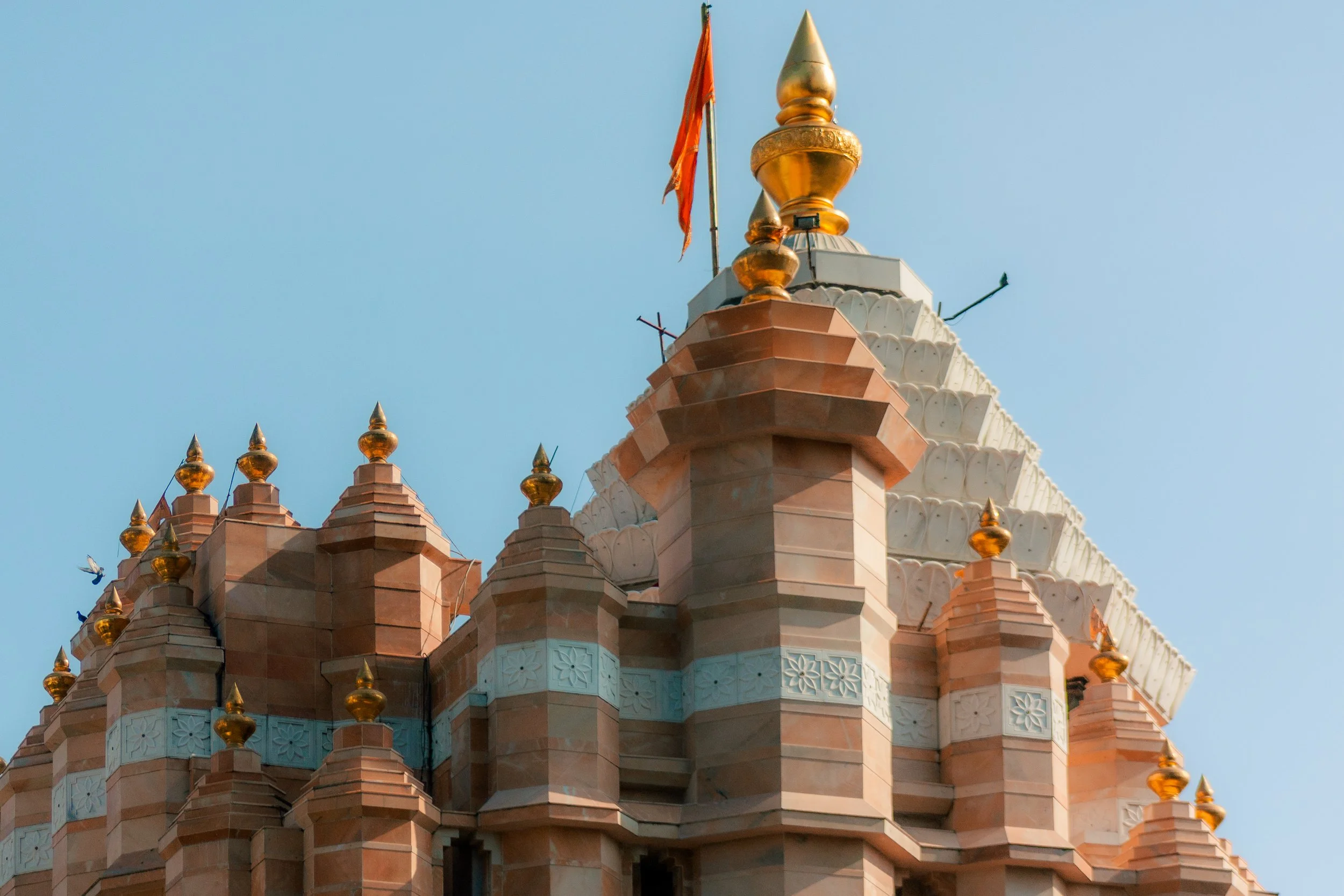 Close-up of a Hindu temple with intricate architecture, golden finials, a flag, and a blue sky background.