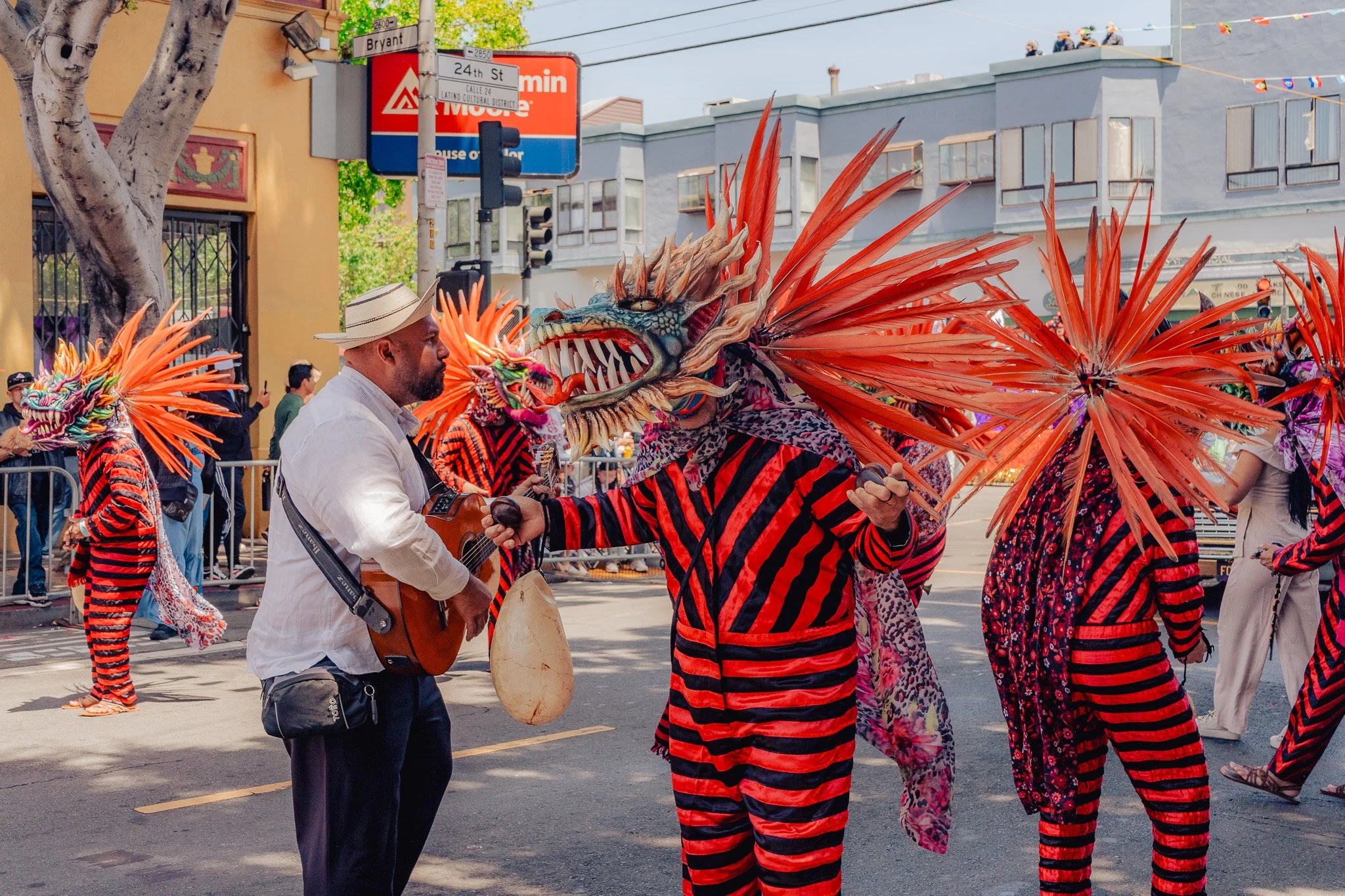 Street scene featuring performers in colorful dragon costumes and a man playing guitar during a parade.