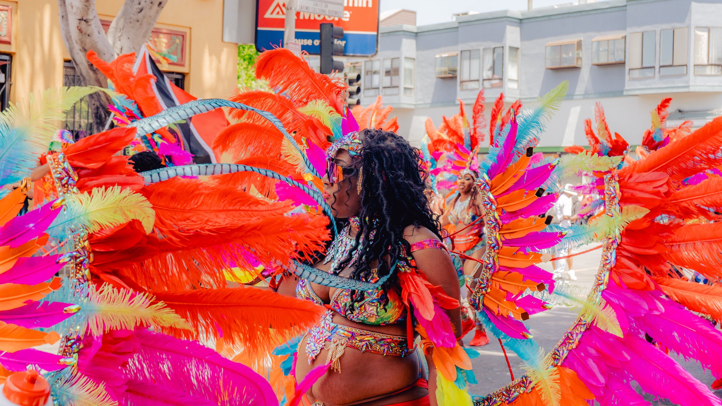 Colorful parade float with women in vibrant feathered costumes during a street celebration.