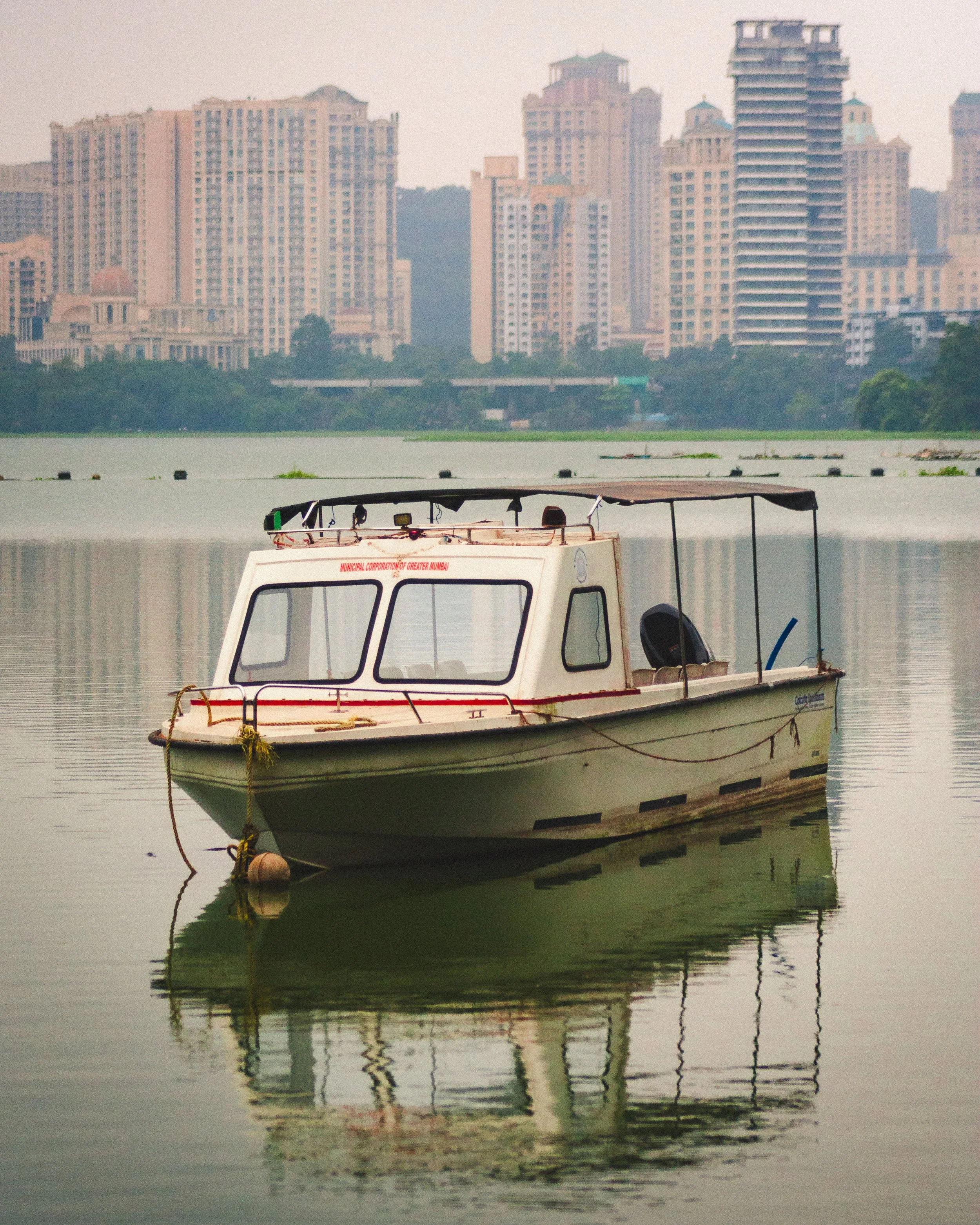 A small boat on calm water with a city skyline of tall buildings in the background.