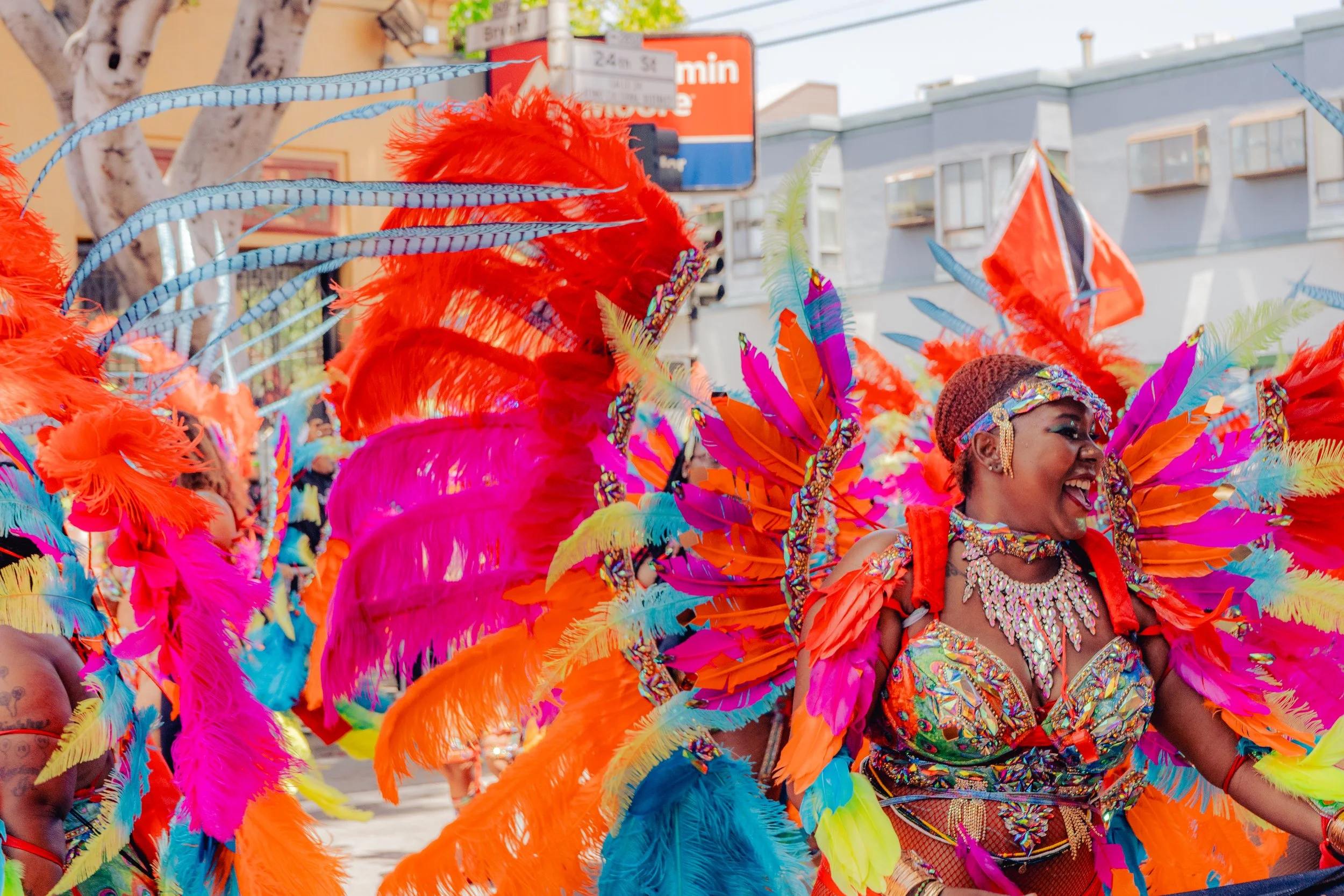 A joyful woman dressed in a colorful carnival costume with bright feathers, beads, and rhinestones, participating in a street parade.