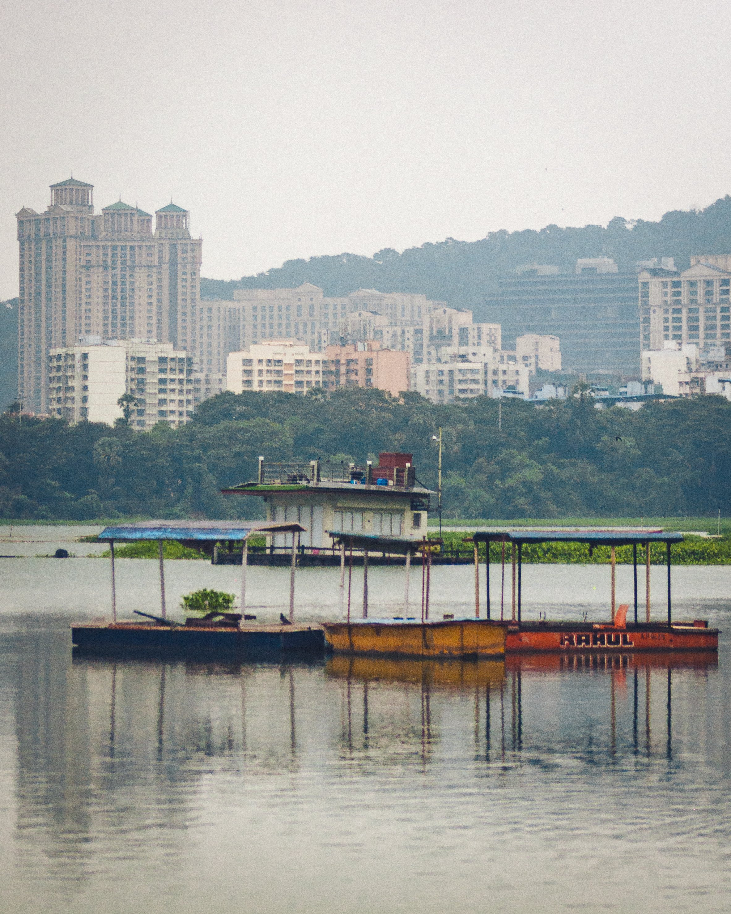 Boats on calm water with city skyline and green hills in the background.