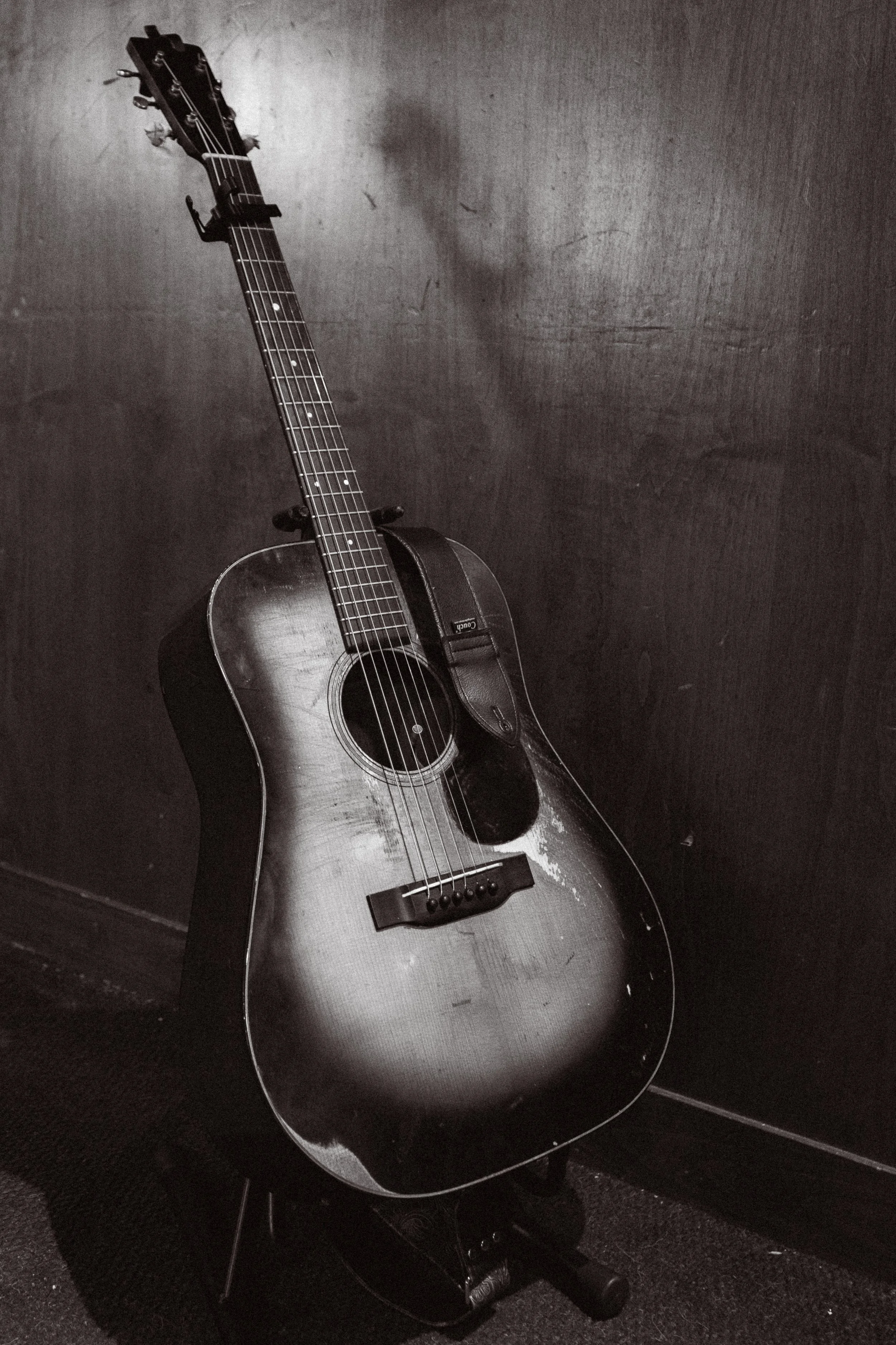 An acoustic guitar with a worn, rustic appearance leaning against a dark wall.