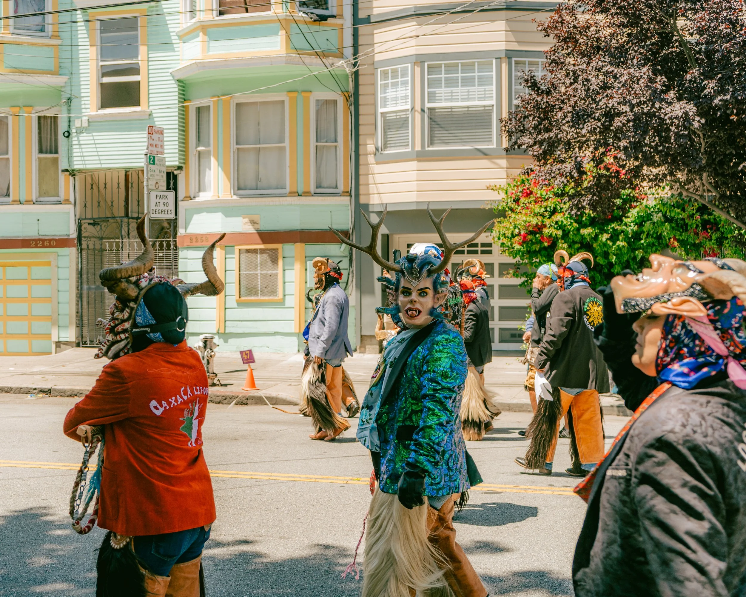People dressed in elaborate costumes with masks, horns, and fur walking down a city street during a parade or festival.
