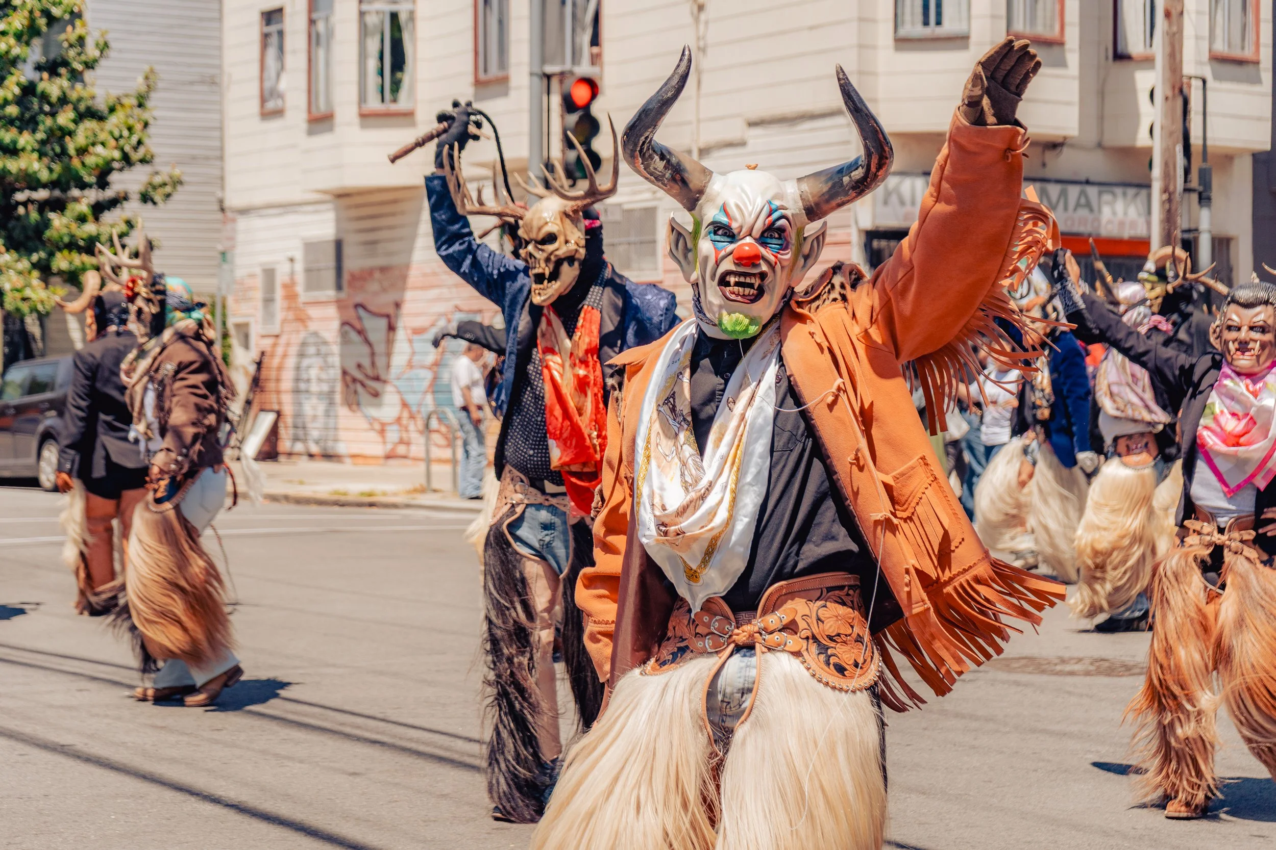 People wearing elaborate costumes with masks, some with animal and demon features, participating in a street parade or festival.
