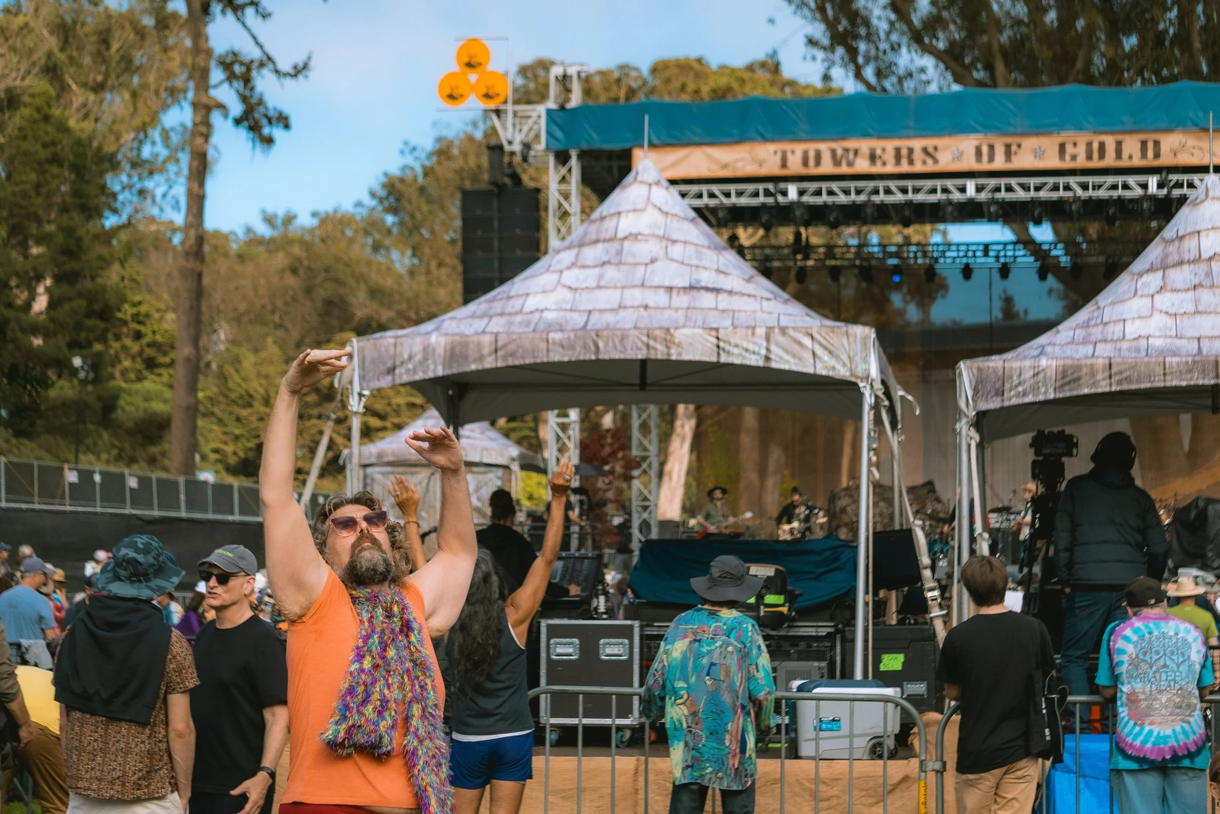 People at an outdoor music festival with a stage and tents, some dancing and enjoying the event.