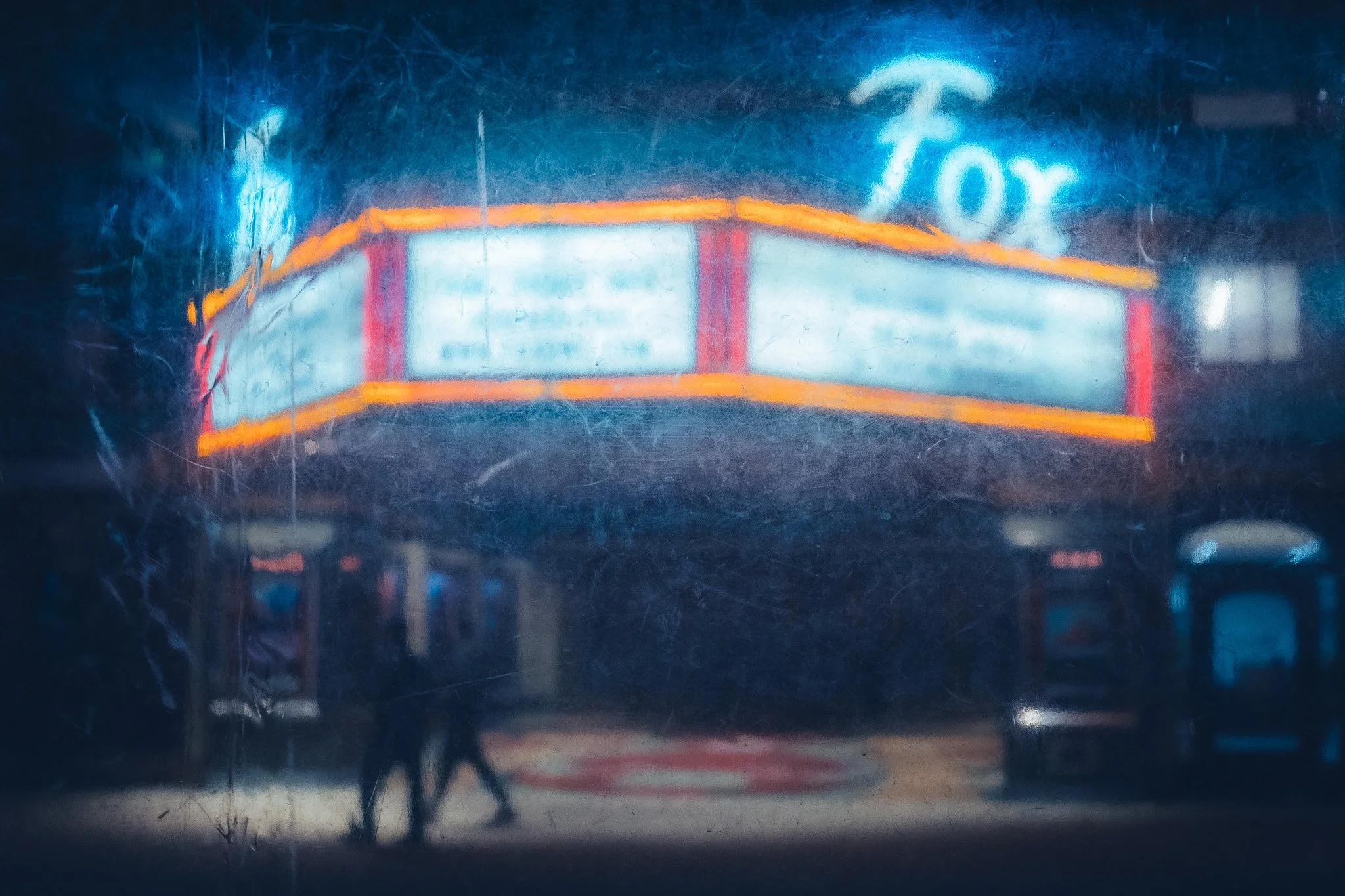 Neon sign for a movie theater with a marquee and a Walk of Fame sign above it, seen through a dirty window.