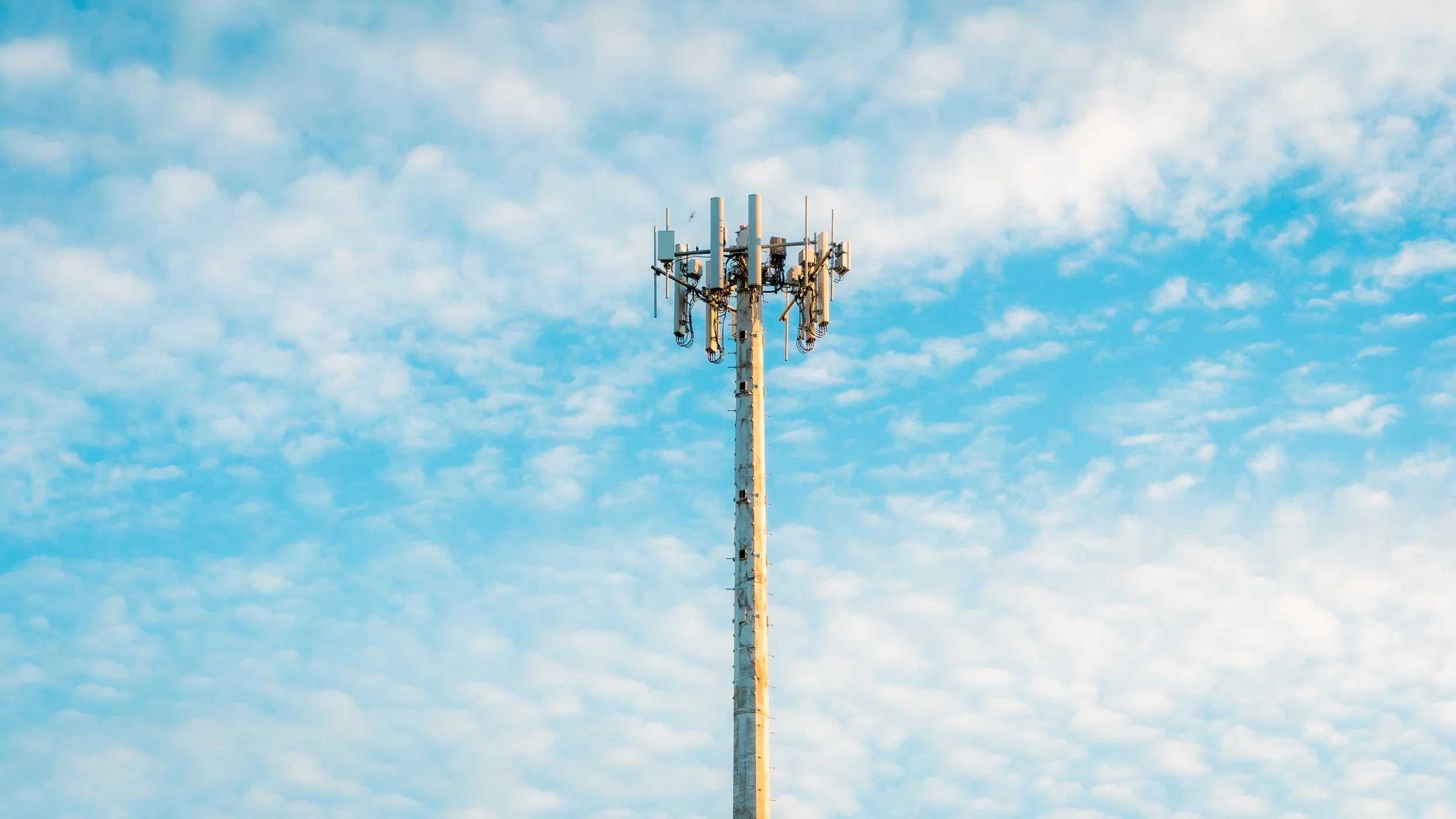 Tower with antenna and multiple signals against a cloudy sky.