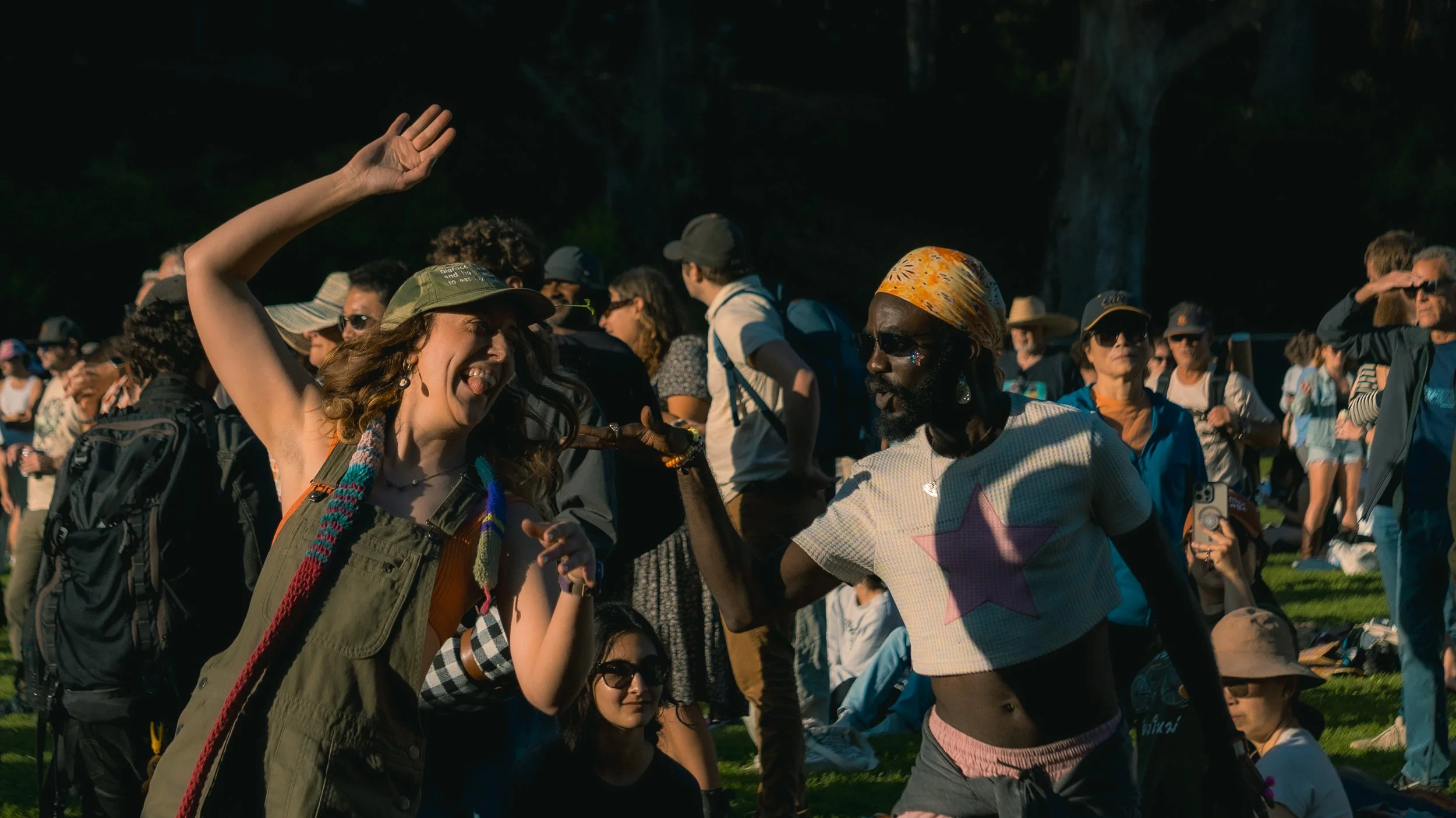 Two women dancing and enjoying music at an outdoor event with a crowd of people in the background.