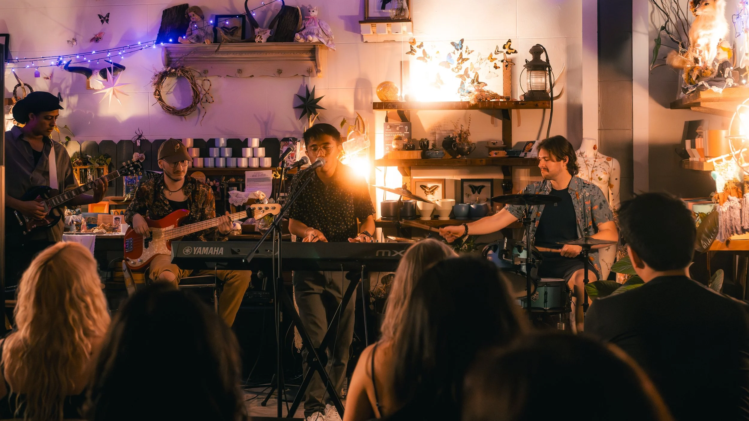 A band performing on stage in a cozy, decorated room with an audience watching.