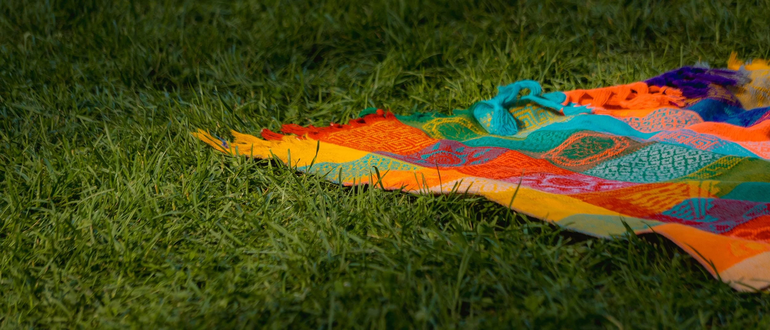 Colorful beach towel with vibrant geometric patterns lying on green grass.