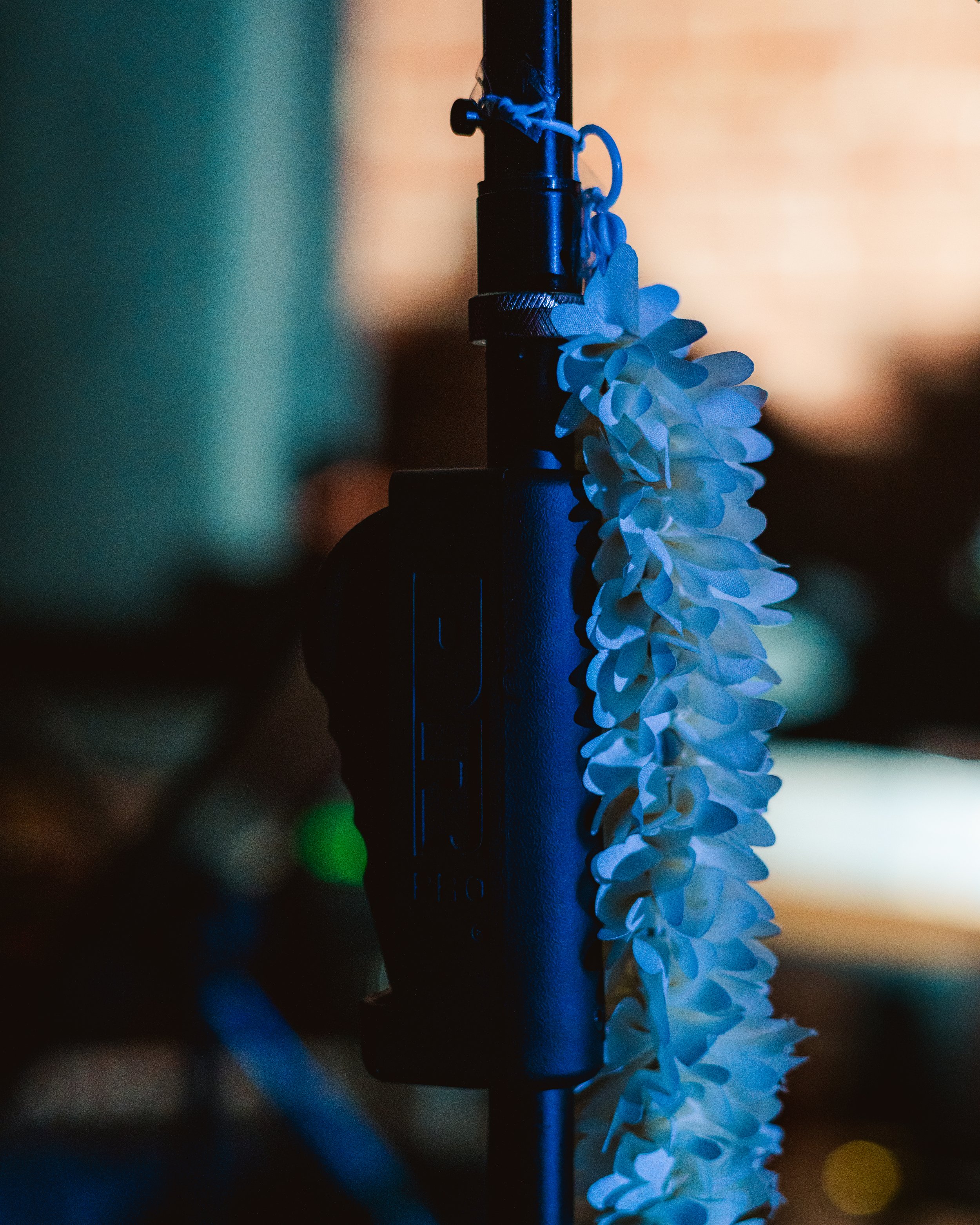 Close-up of a black microphone with a string of white flowers hanging beside it, illuminated by soft blue lighting.