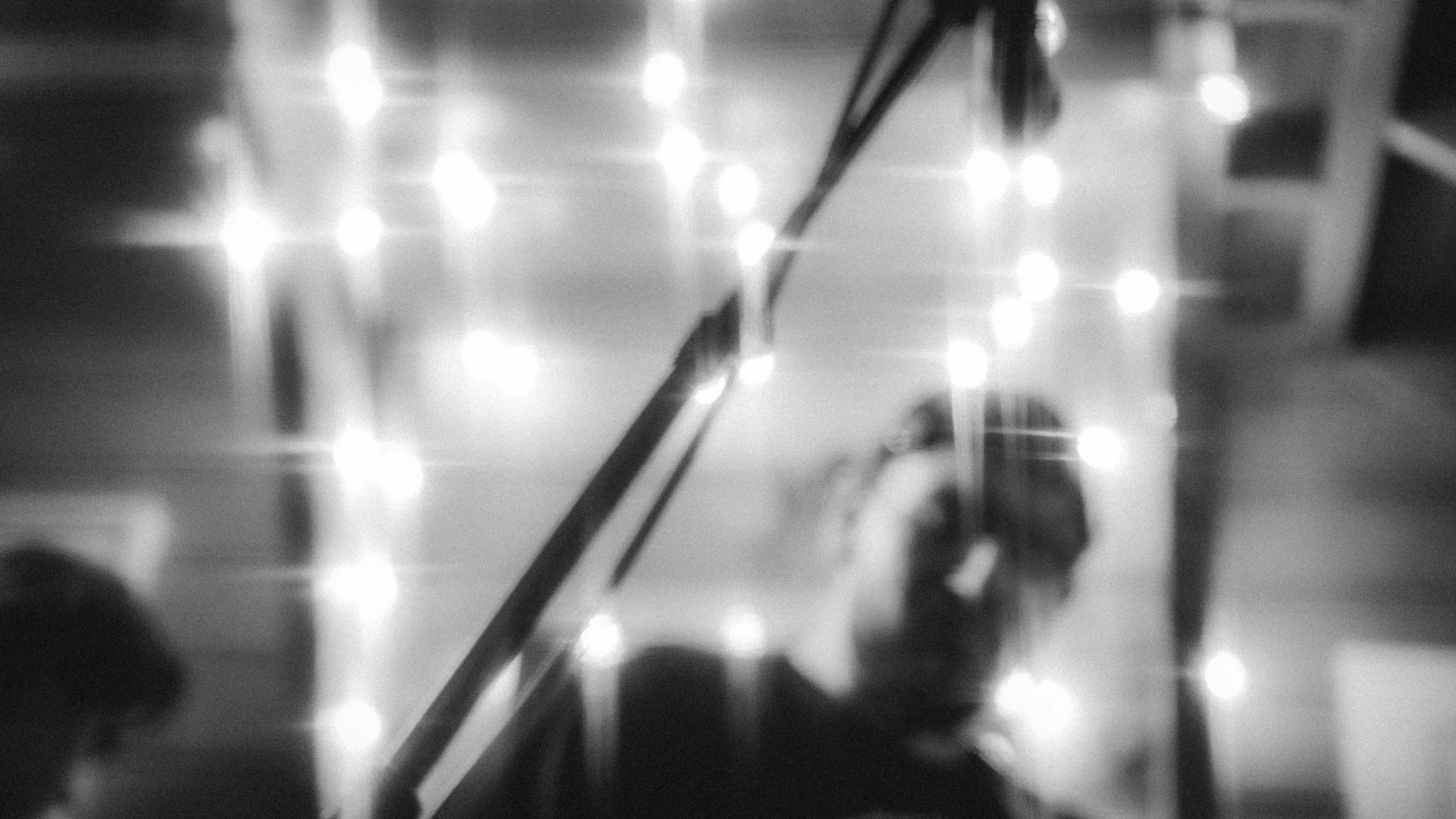 Black-and-white photo of an elevator reflection showing a person taking a picture with a phone, floor lights, and railing.