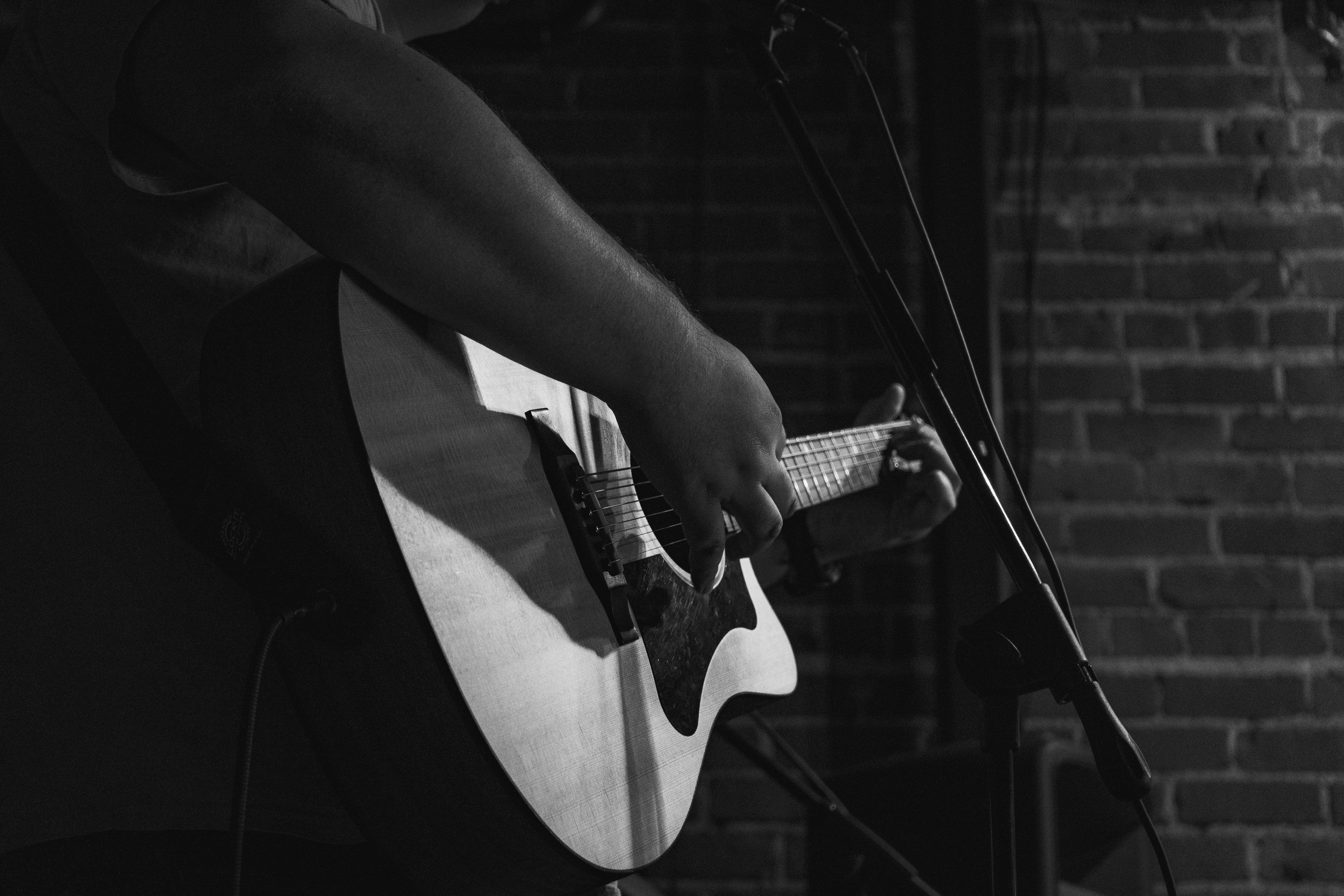 A person playing an acoustic guitar near a brick wall, with a microphone nearby.