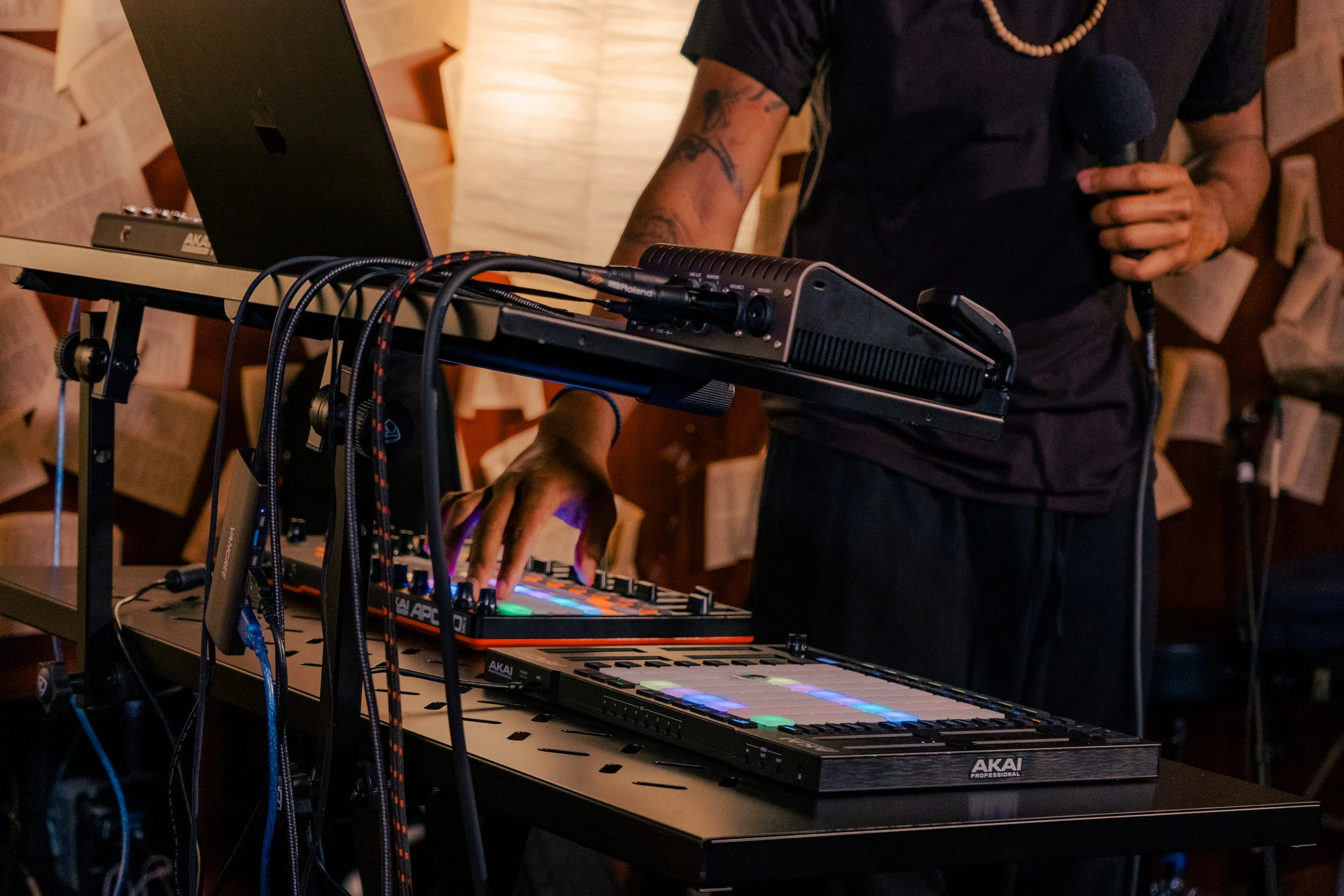 A person operating DJ equipment with a laptop and a microphone, with walls decorated with open books.