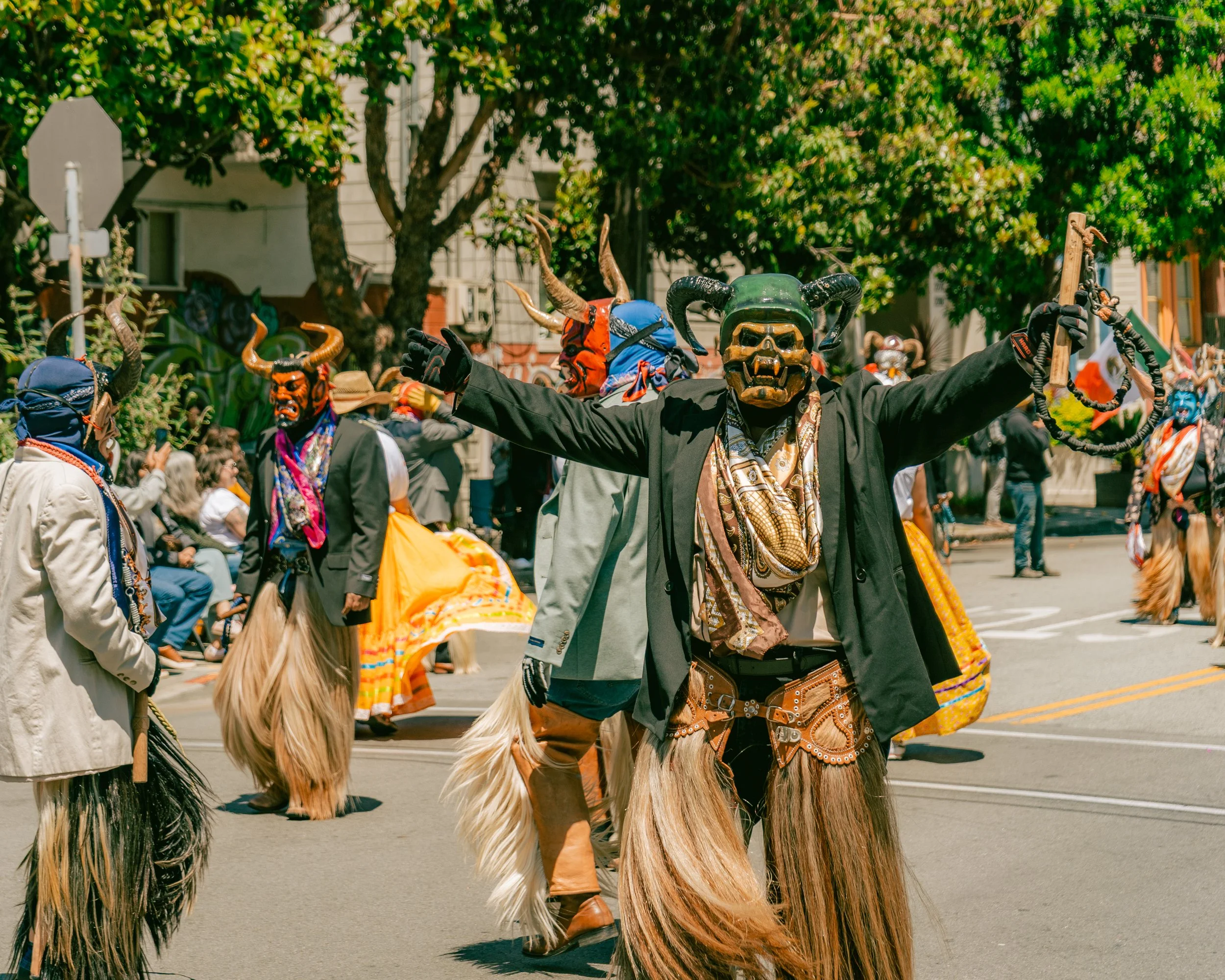 People in colorful costumes and masks participating in a parade or festival on a city street.