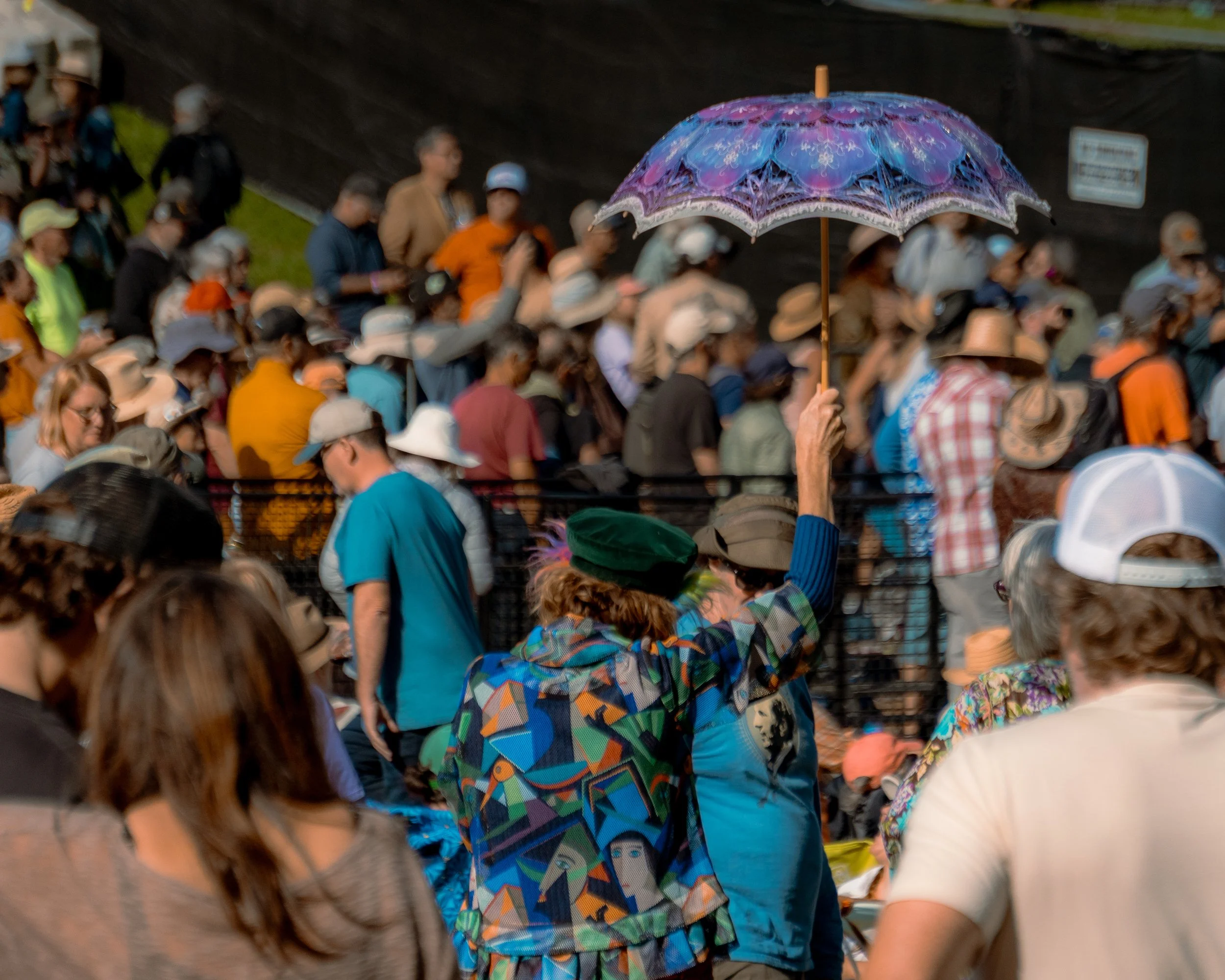 A large crowd of people gathered outdoors, with one person holding a purple patterned umbrella.
