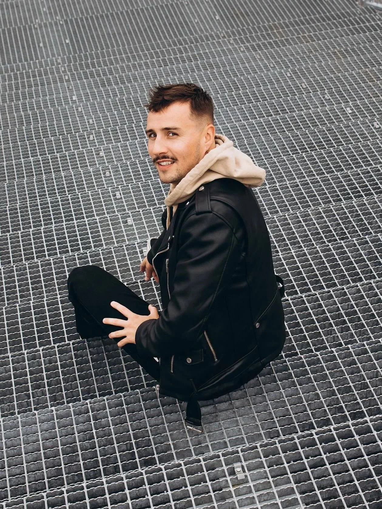 Pesojoonas istuu metallirampilla katsoen kameraan, rennosti hymyillen, pää hieman kääntyneenä oikealle.