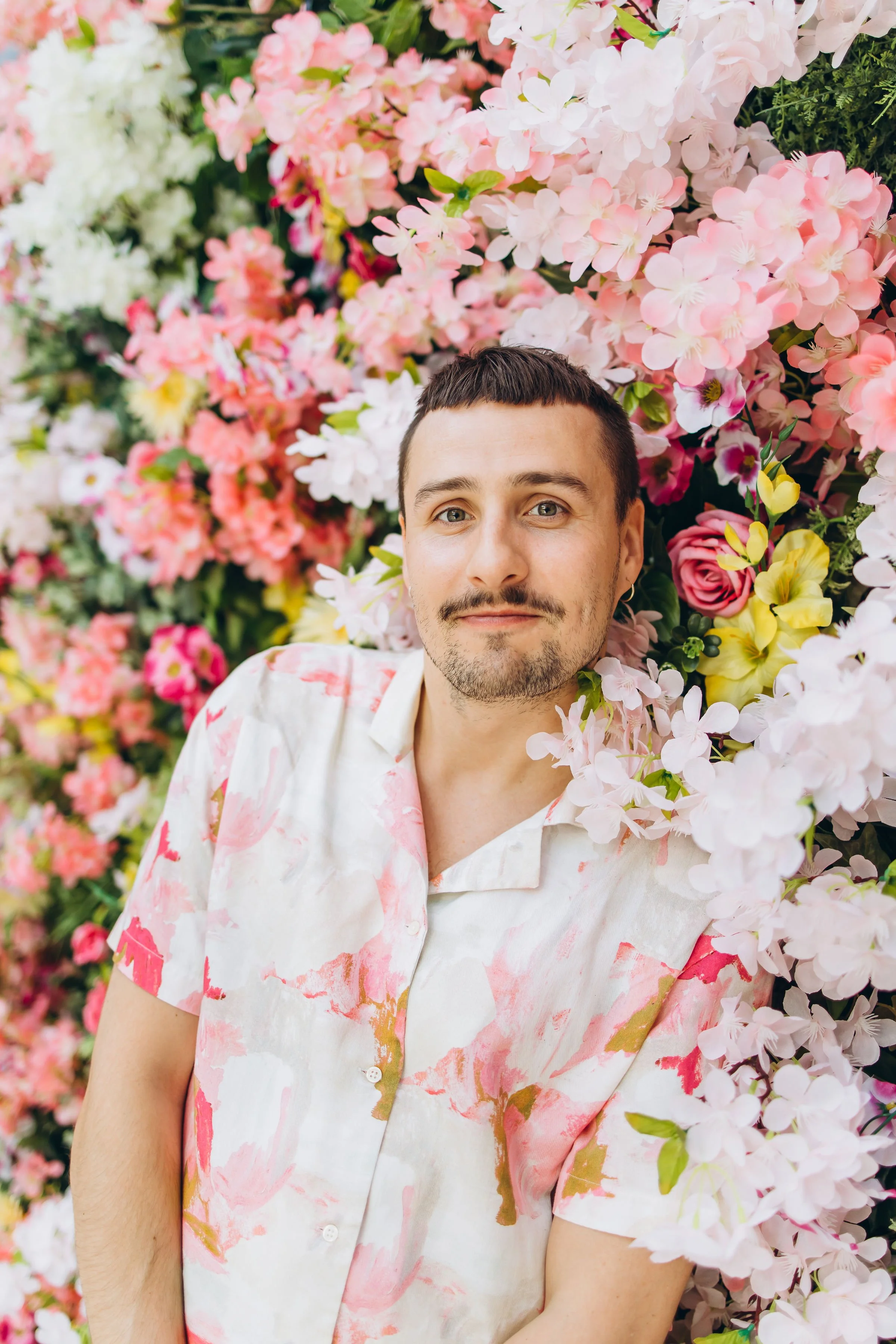 Lähikuva Pesojoonaksesta seisoo kukkivien värikkäiden kukkien edessä hymyillen.