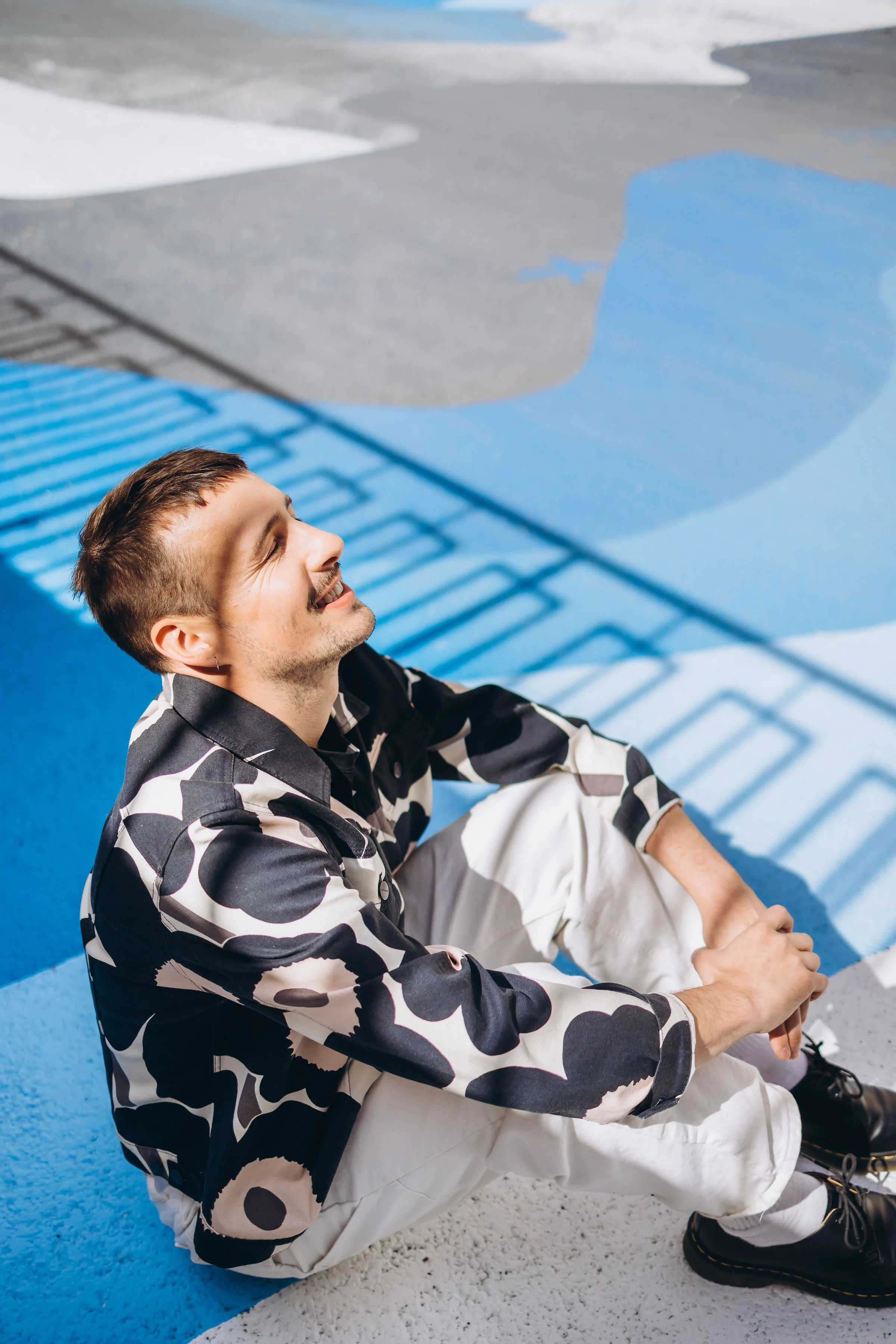 Pesojoonas istuu maassa hymyillen, taustalla värikäs maalaus betoniseinällä.